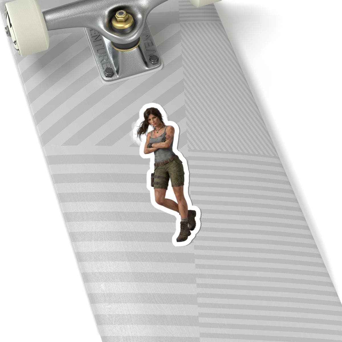 May include: A sticker featuring a digital illustration of a woman in a gray tank top, green shorts, and brown boots. The sticker is placed on a skateboard with a gray and white striped pattern.