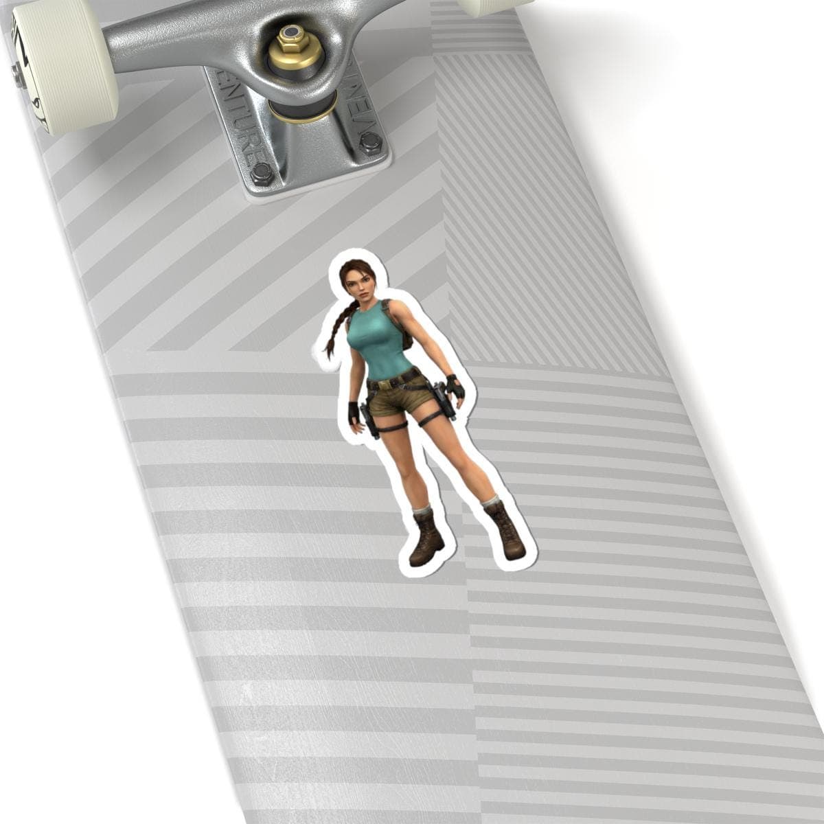 May include: A sticker featuring a character from the Tomb Raider video game series. The character is depicted in a teal tank top, brown shorts, and boots, with black accessories. The sticker is placed on a skateboard.