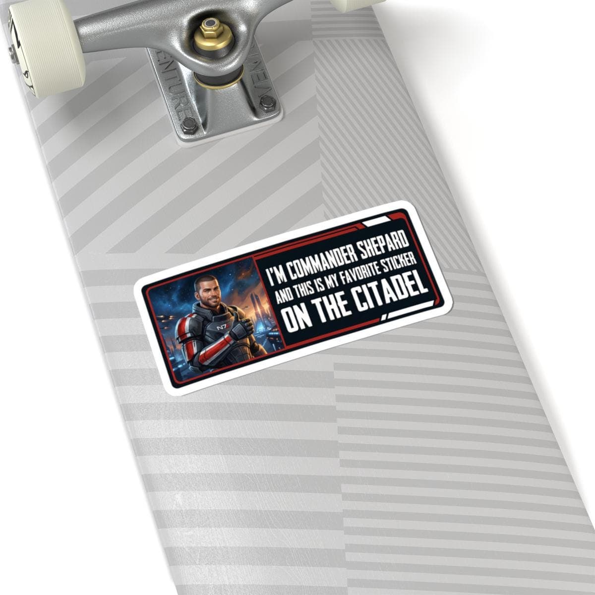 May include: Rectangular sticker featuring a portrait of Commander Shepard from Mass Effect, with text that reads "I'M COMMANDER SHEPARD AND THIS IS MY FAVORITE STICKER ON THE CITADEL". The sticker has a white border and is on a skateboard.