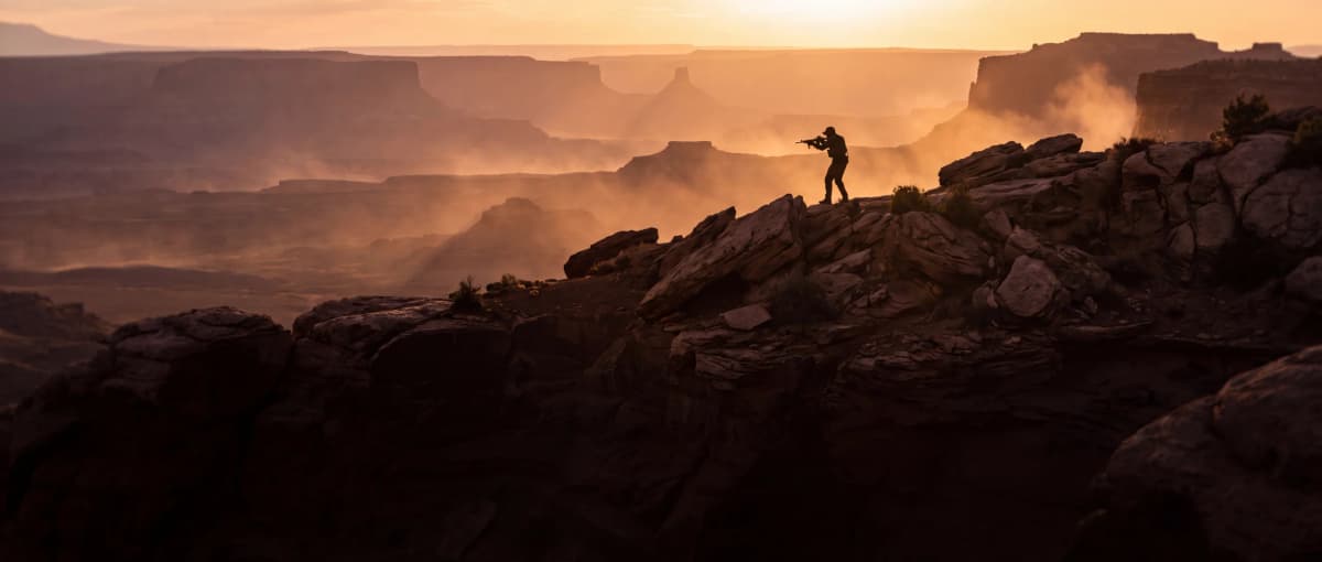 Rifleman silhouetted on a desert ridgeline at golden hour carrying an AR-15