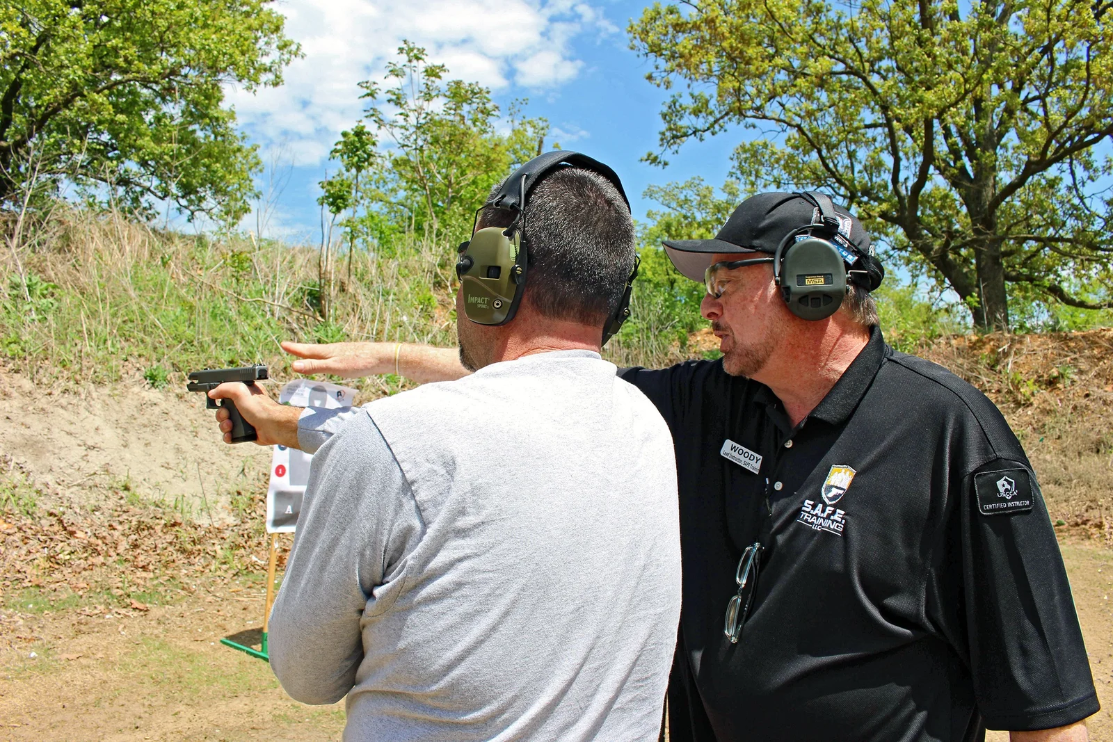 Firearms instructor coaching a handgun student at an outdoor range