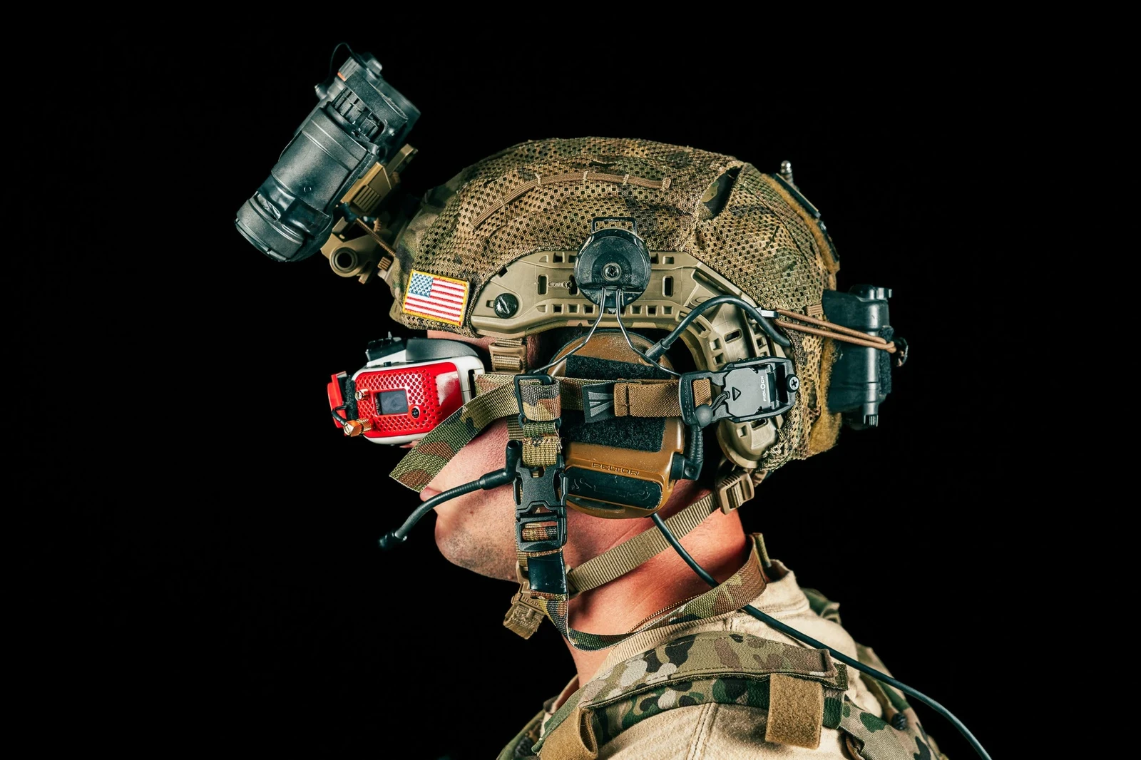 Side profile of a helmeted operator with the FPV goggle released and hanging at chest level on the neckband safety strap while a night vision device sits flipped up on the shroud