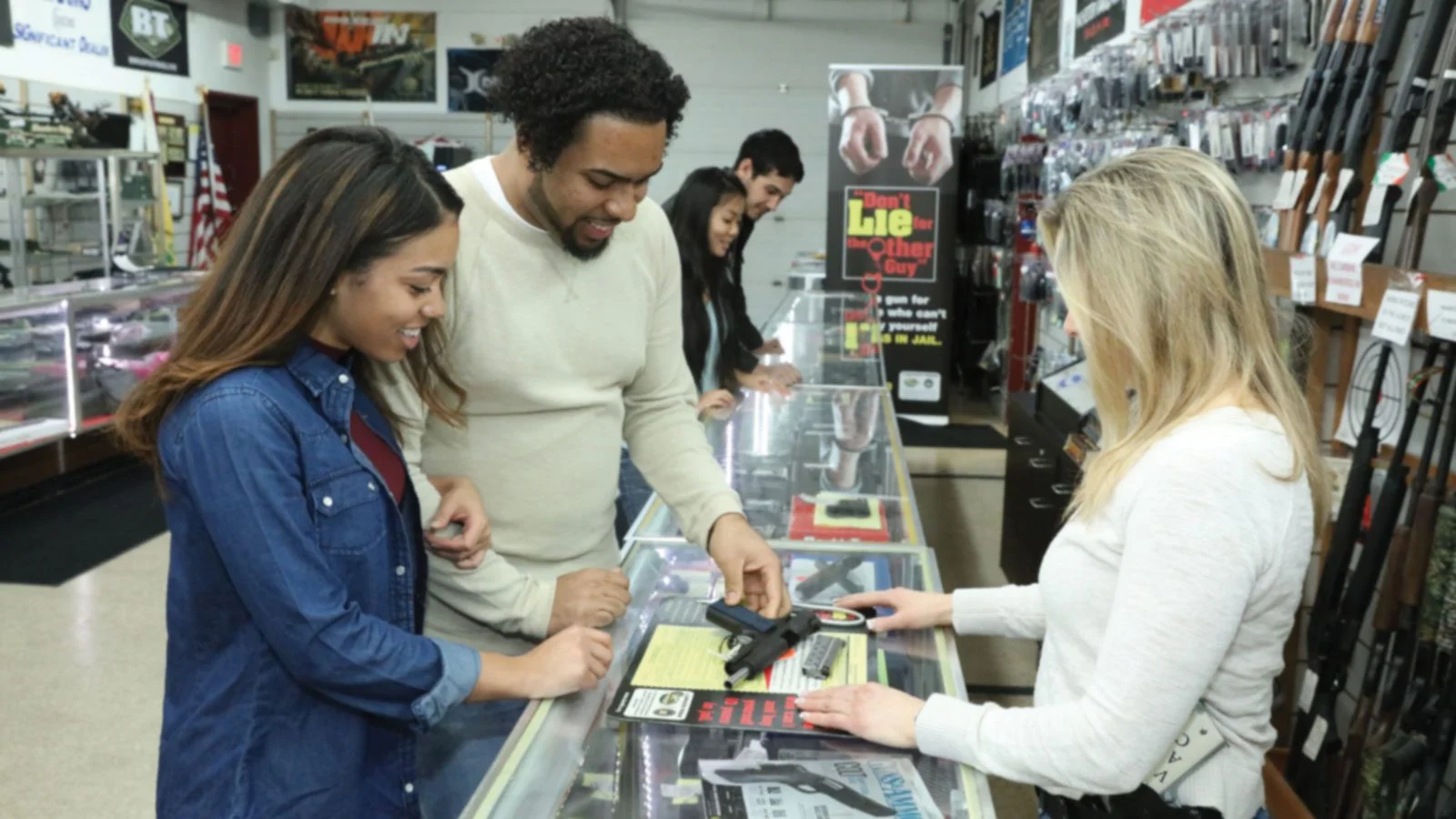 Customers speaking with a firearms retailer across a gun shop display counter