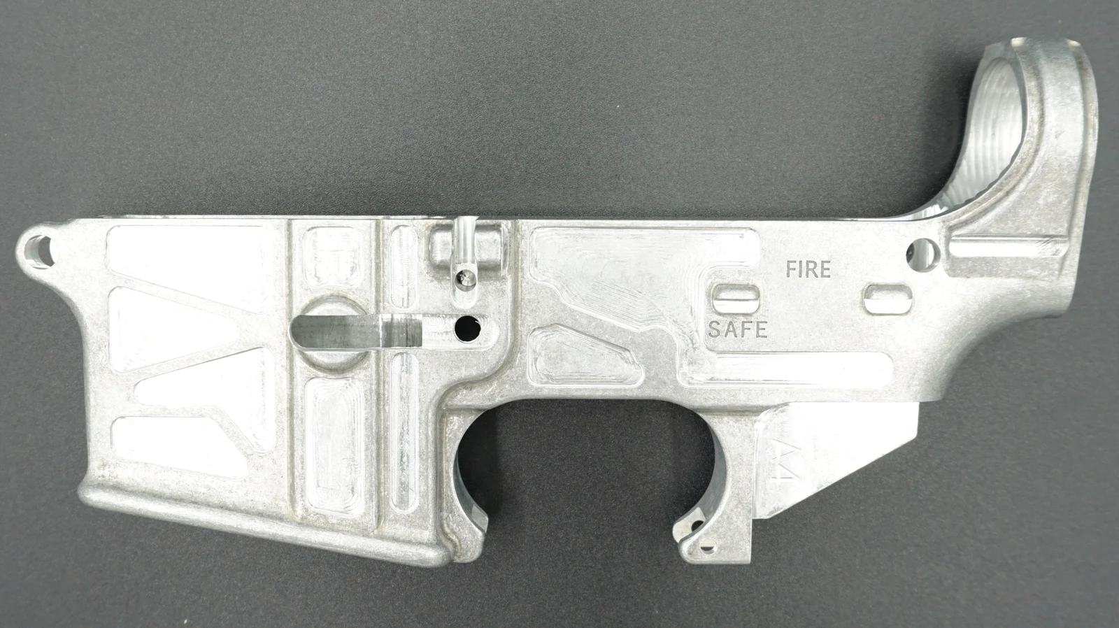 Raw unfinished billet AR-15 80 percent lower receiver with an unmachined fire control pocket, laid on a dark surface