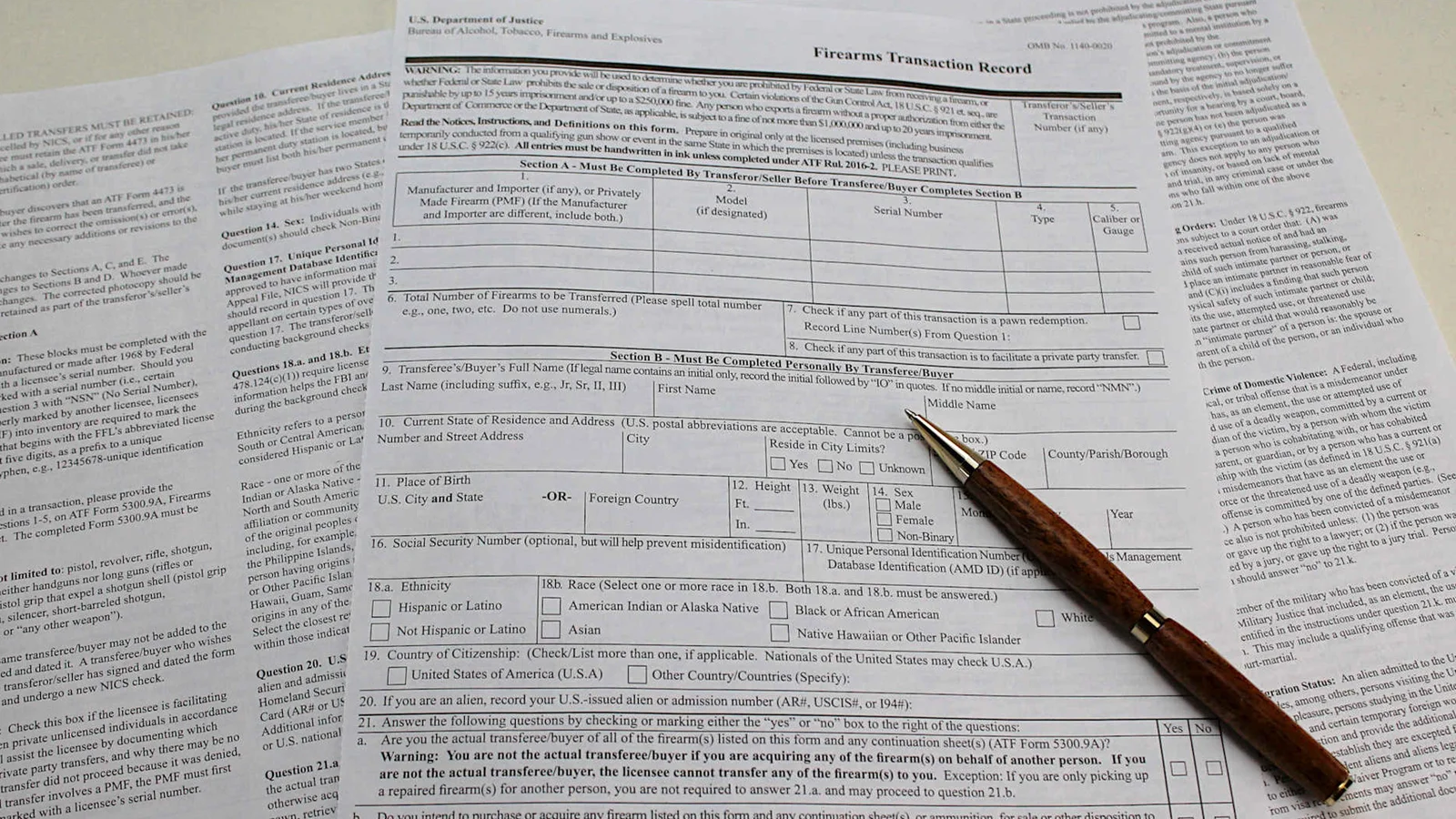 ATF Form 4473 Firearms Transaction Record laid out on a counter with the instruction pages beside it and a pen resting on the form