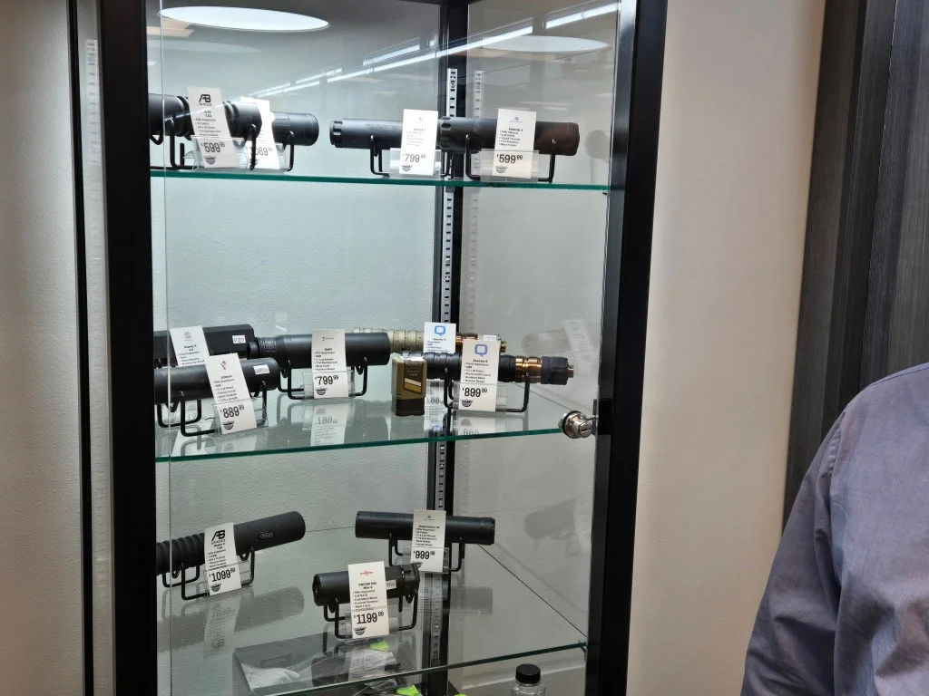 Glass display case of suppressors with price tags on three shelves in a gun store
