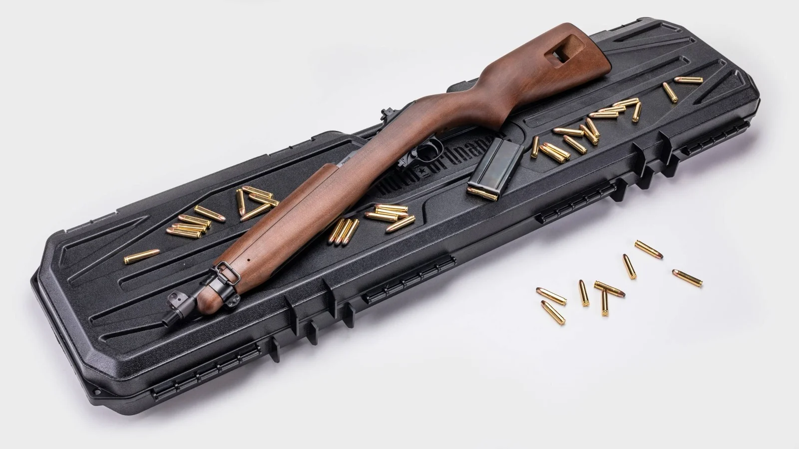 Auto-Ordnance M1 Carbine SBR resting diagonally on a closed black hard rifle case, surrounded by loose .30 Carbine cartridges with a detachable box magazine