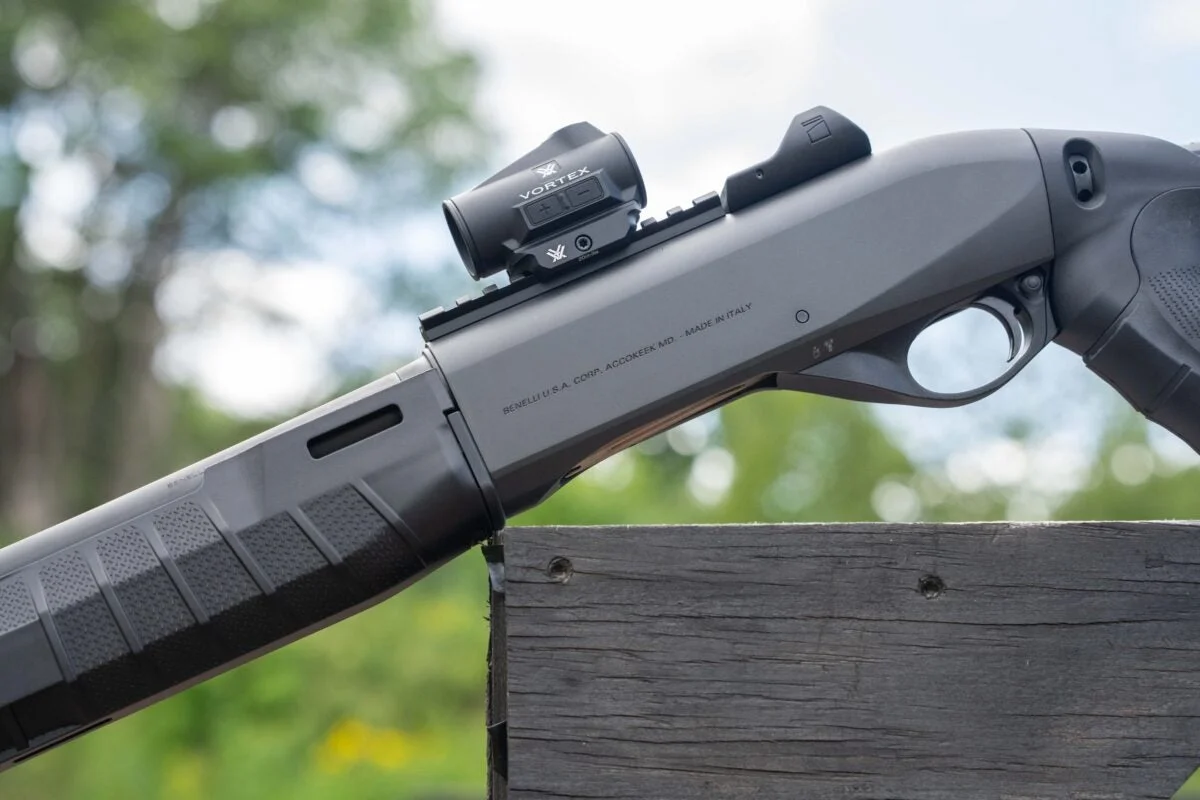 Gray Benelli M2-G1 Tactical with a Vortex red dot mounted on the receiver rail, resting on a wooden barricade