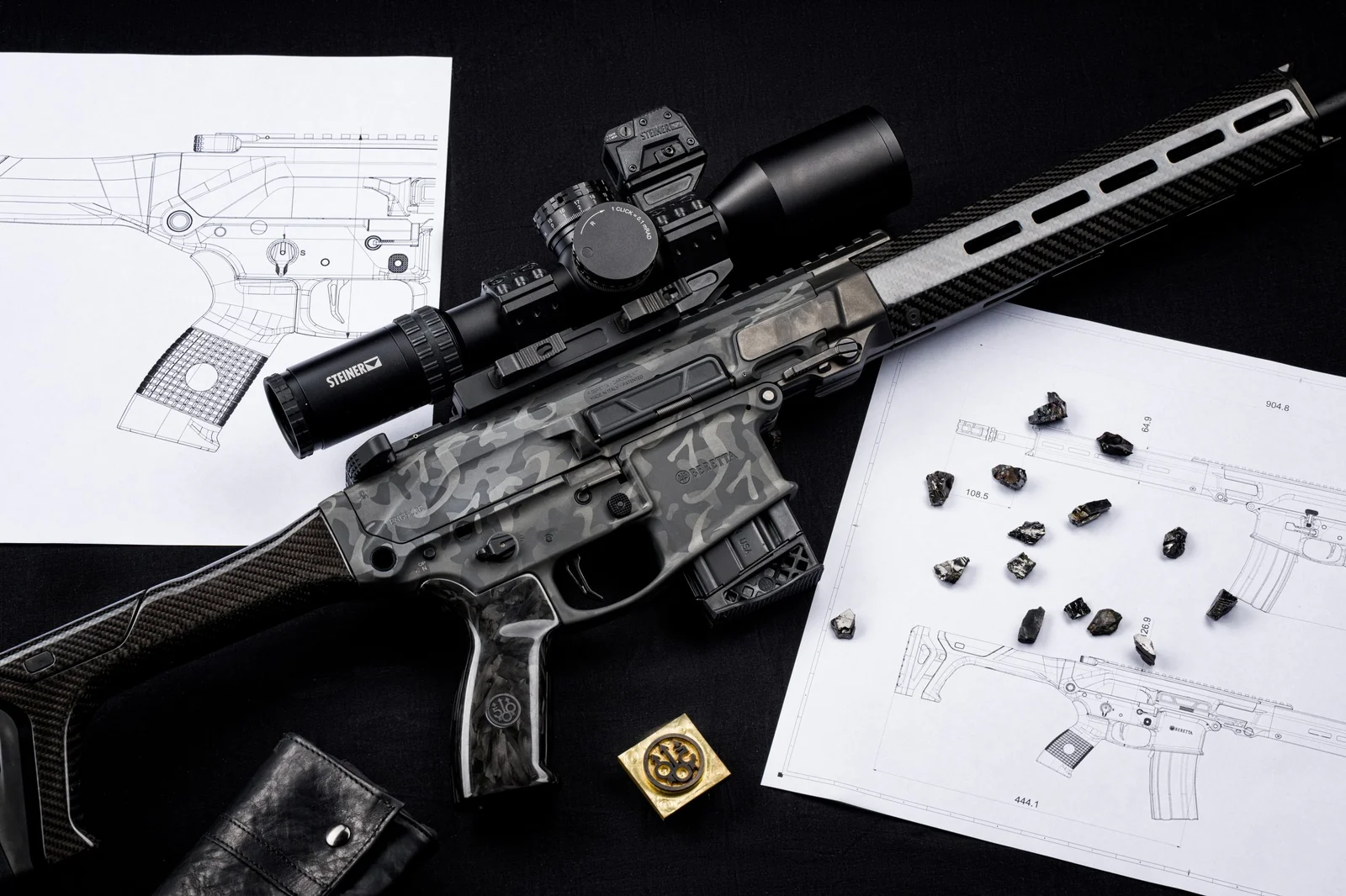 Overhead flatlay of the Beretta Titan modern sporting rifle with carbon fiber components, blueprints, and material samples laid out on a black surface