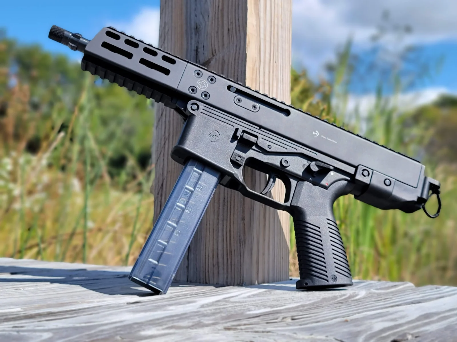 B&T GHM9 9mm pistol with M-LOK handguard and translucent B&T magazine leaning against a wooden post
