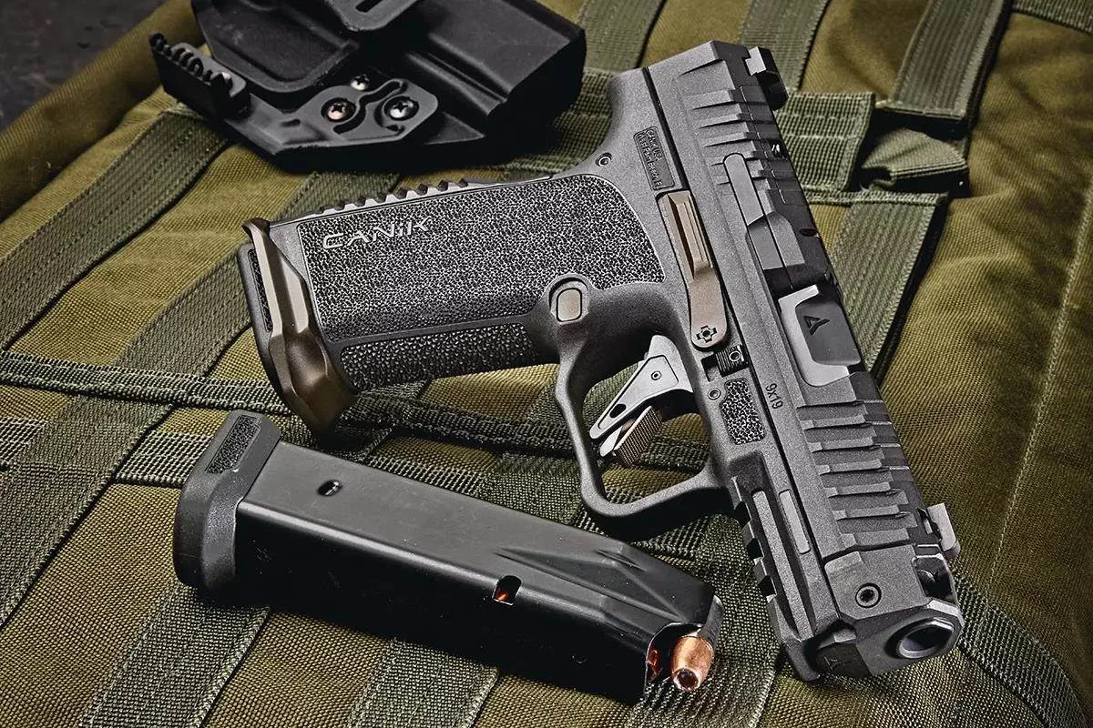 CANiK Prime Radian 9mm pistol resting on a green tactical bag next to a loaded magazine and holster, showing the Radian BACKSTRAP+MAGWELL grip module