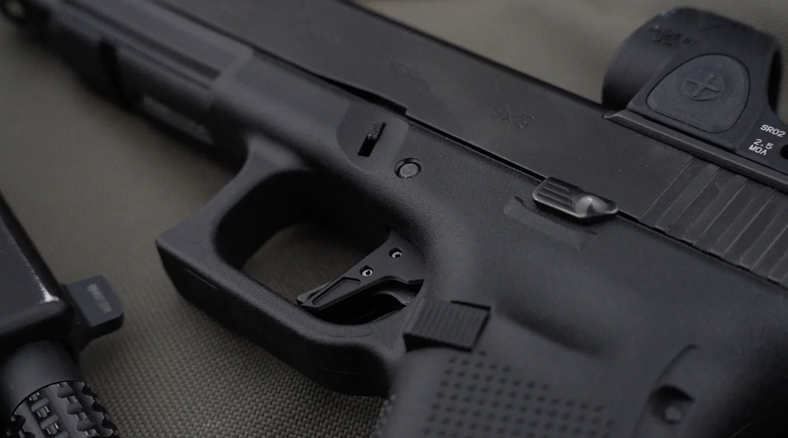 Close-up of a Glock-pattern pistol with a flat-face aftermarket trigger and a slide-mounted red dot