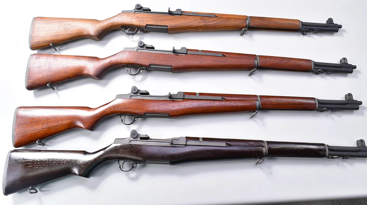 Four M1 Garand rifles with walnut stocks laid out side by side