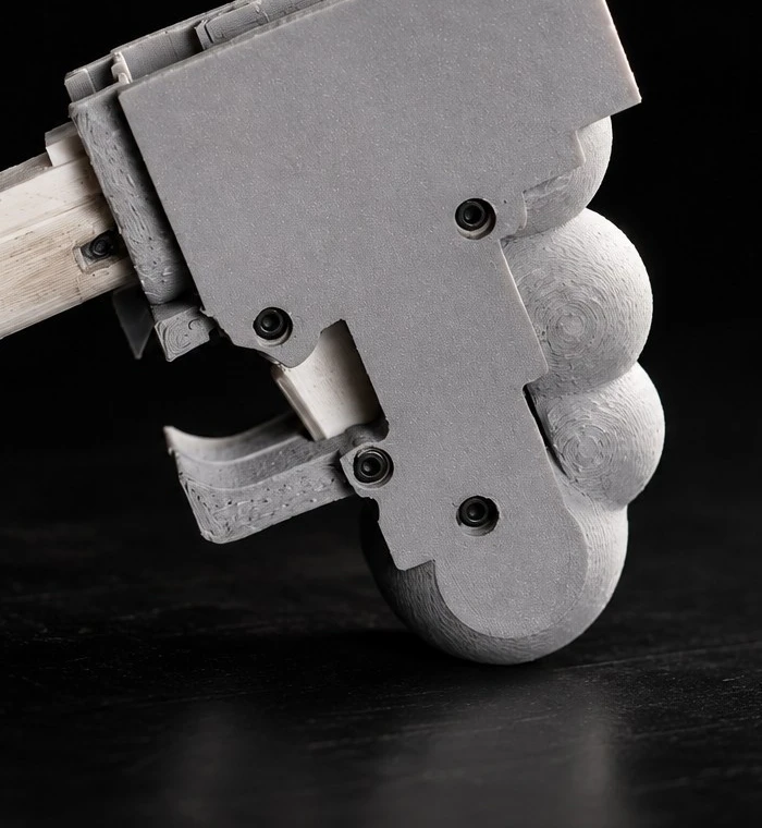 Close-up of the gray 3D-printed WASP handgun showing its three-lobed grip, exposed trigger, and partial trigger guard