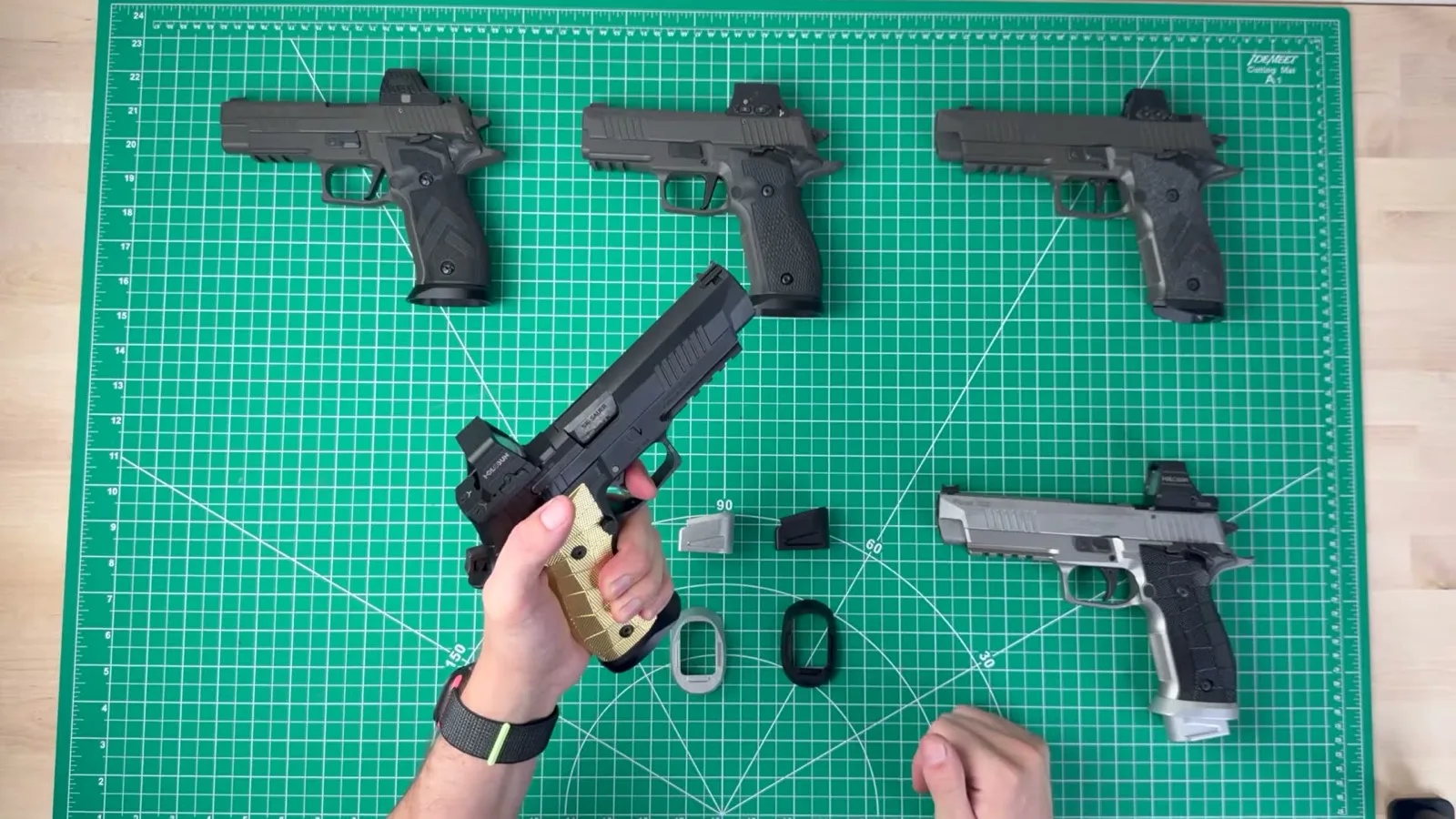 SIG P226 X-Five fitted with brass LOK GridLOK grip panels, held above a bench with the raw and black Cascade Range Systems magwells laid out below
