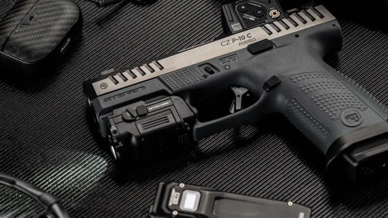 CZ P-10 C Ported COA with weapon light on carbon fiber surface, showing ported barrel, extended serrations, and Aimpoint COA