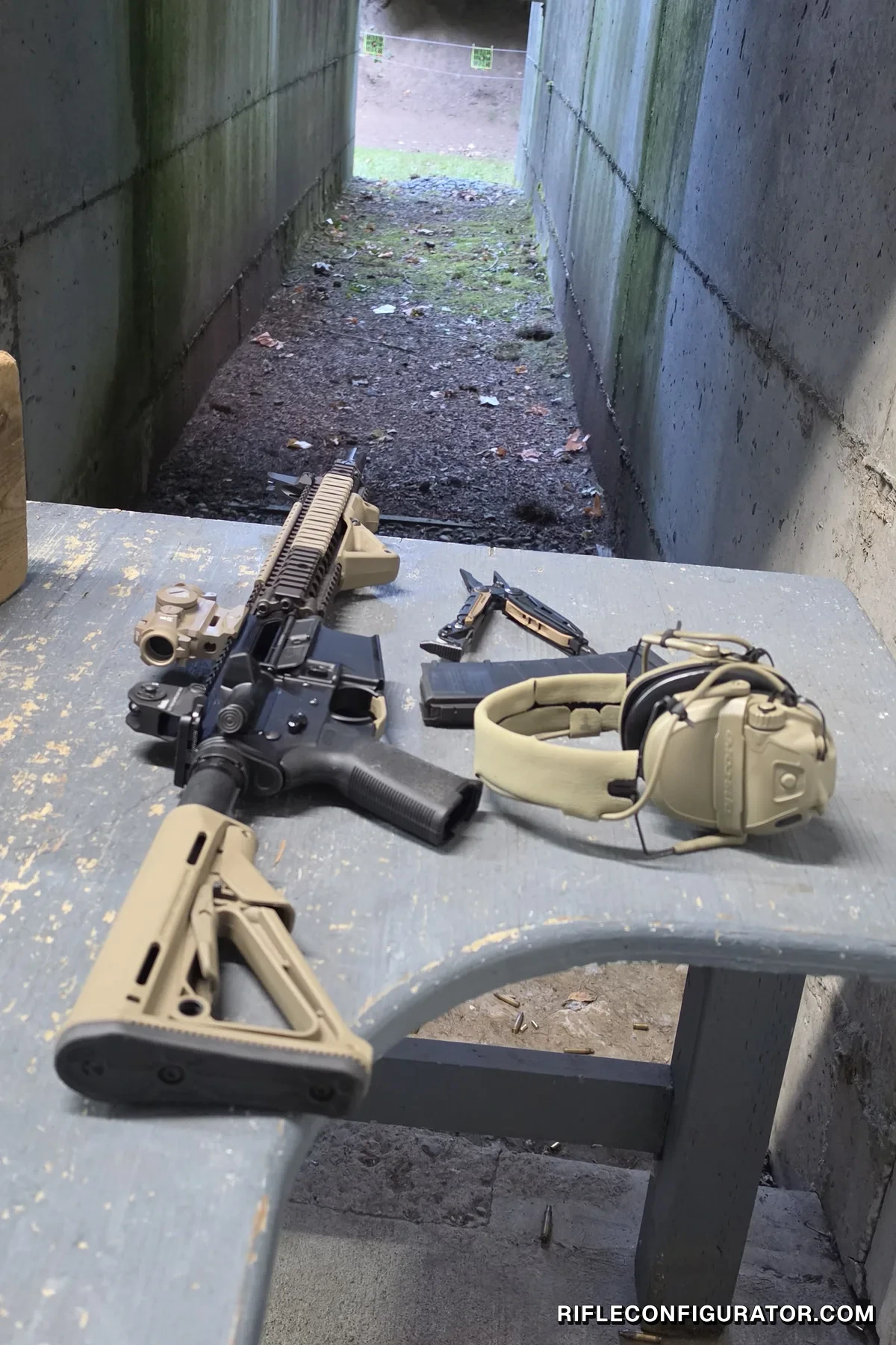 The Block II carbine resting on a covered concrete range bench beside a loaded PMAG, electronic ear protection, and a multitool, with the shooting lane and target frames visible downrange