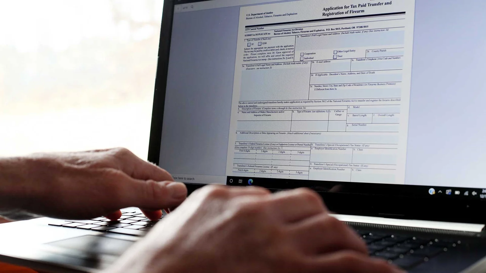 Hands typing on a laptop displaying the ATF Form 4 Application for Tax Paid Transfer and Registration of Firearm