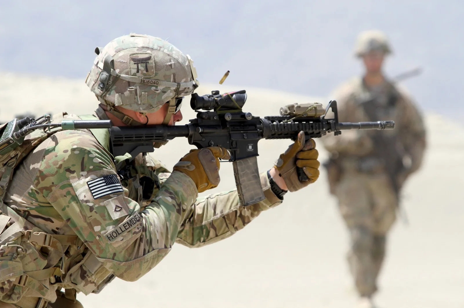 A U.S. Army soldier in OCP camouflage firing an M4 carbine with an ACOG optic, illustrating the dismounted small-arms context the Peak Alloy license supports