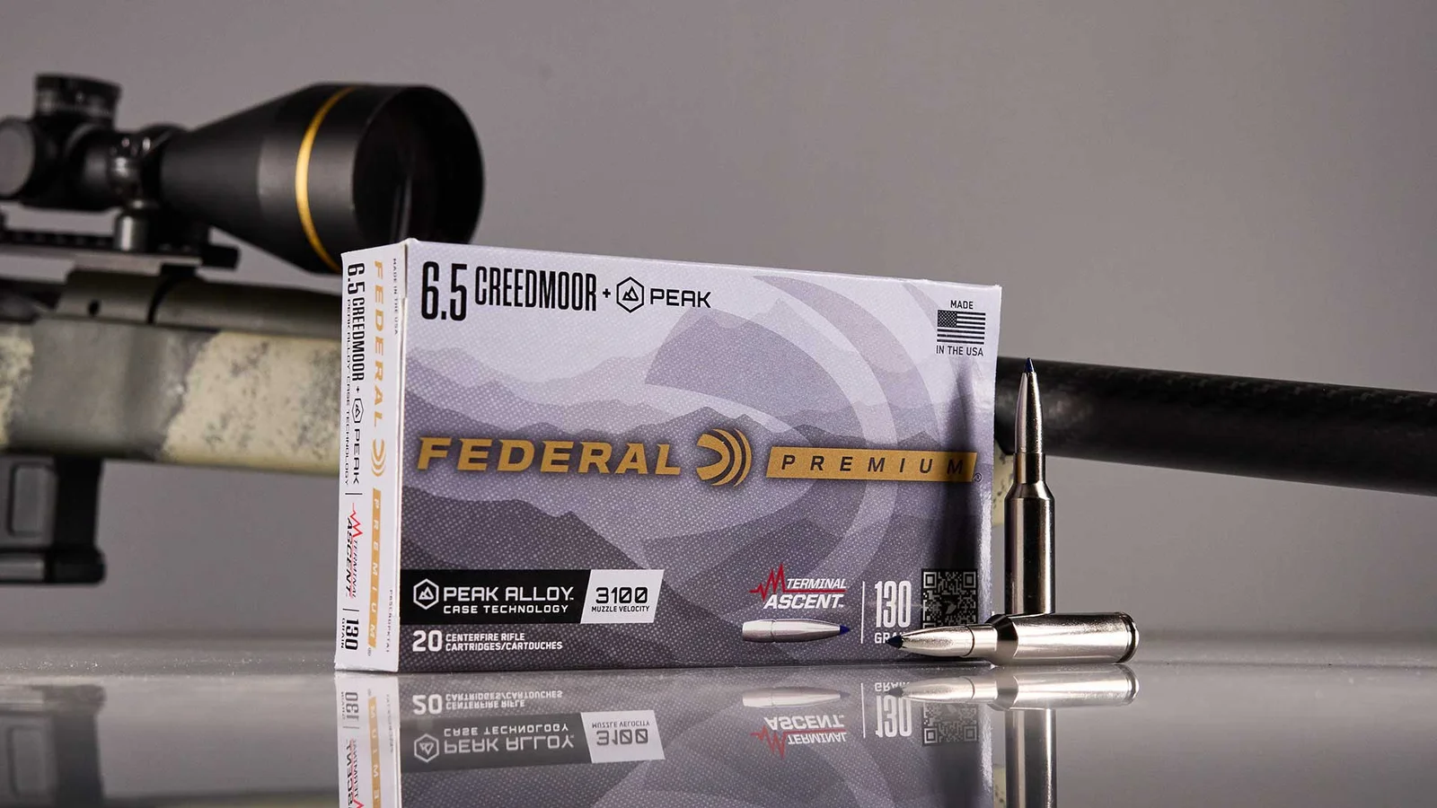 A Federal Premium ammunition box featuring the Peak Alloy Case Technology branding alongside loaded cartridges and a rifle in the background