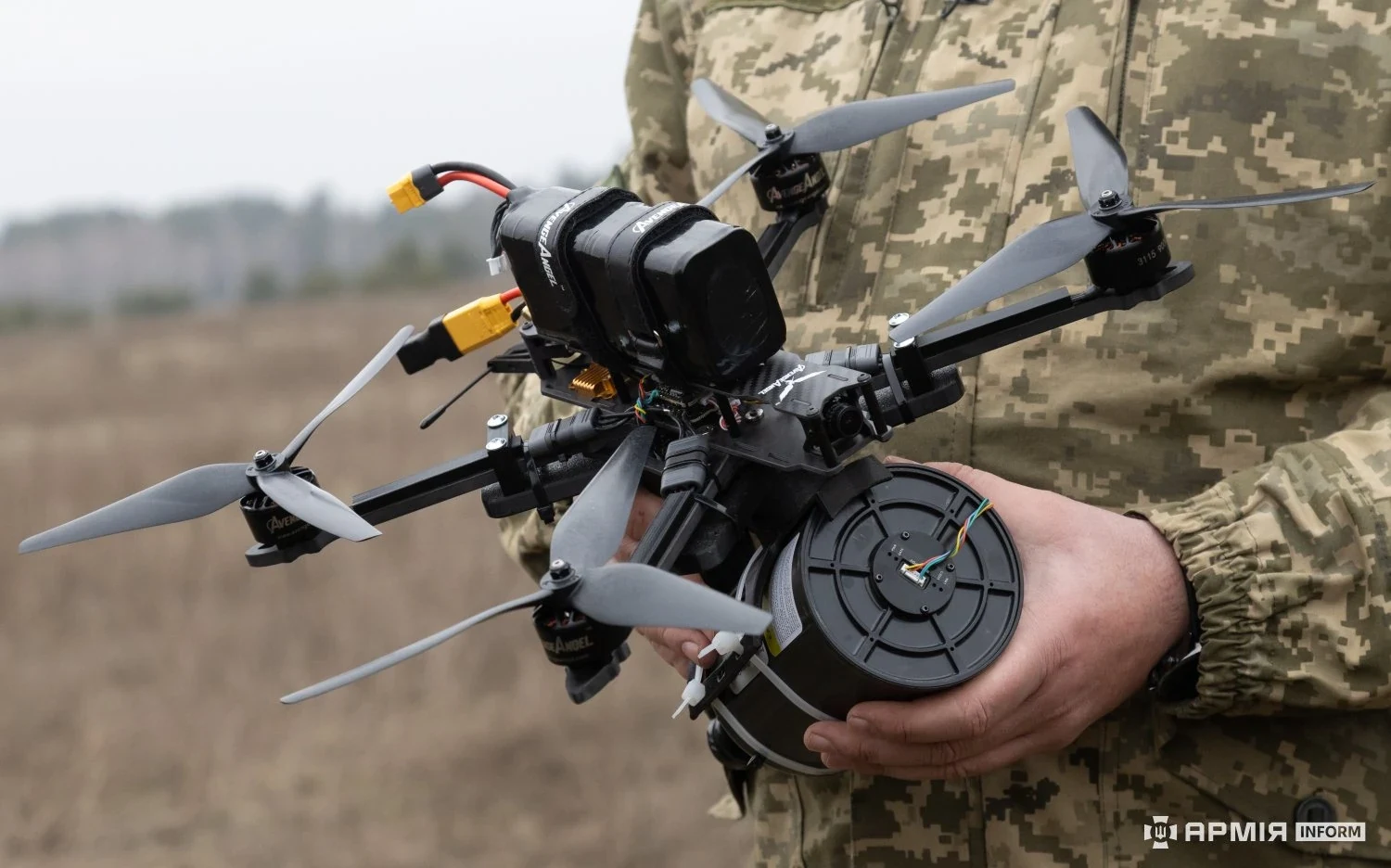 Ukrainian soldier holding a fiber-optic FPV quadcopter, with the black cylindrical fiber spool canister mounted under the airframe
