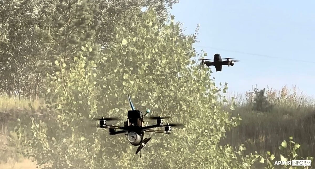 Two Ukrainian FPV strike drones flying low over a treeline in daylight