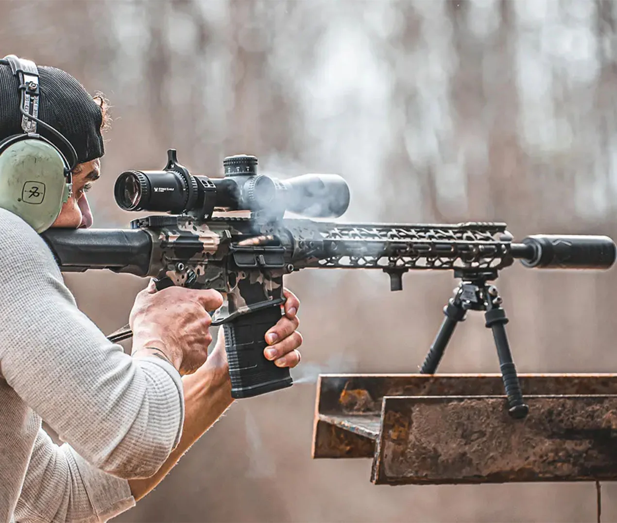 A suppressor on a rifle in a range setting next to hearing protection