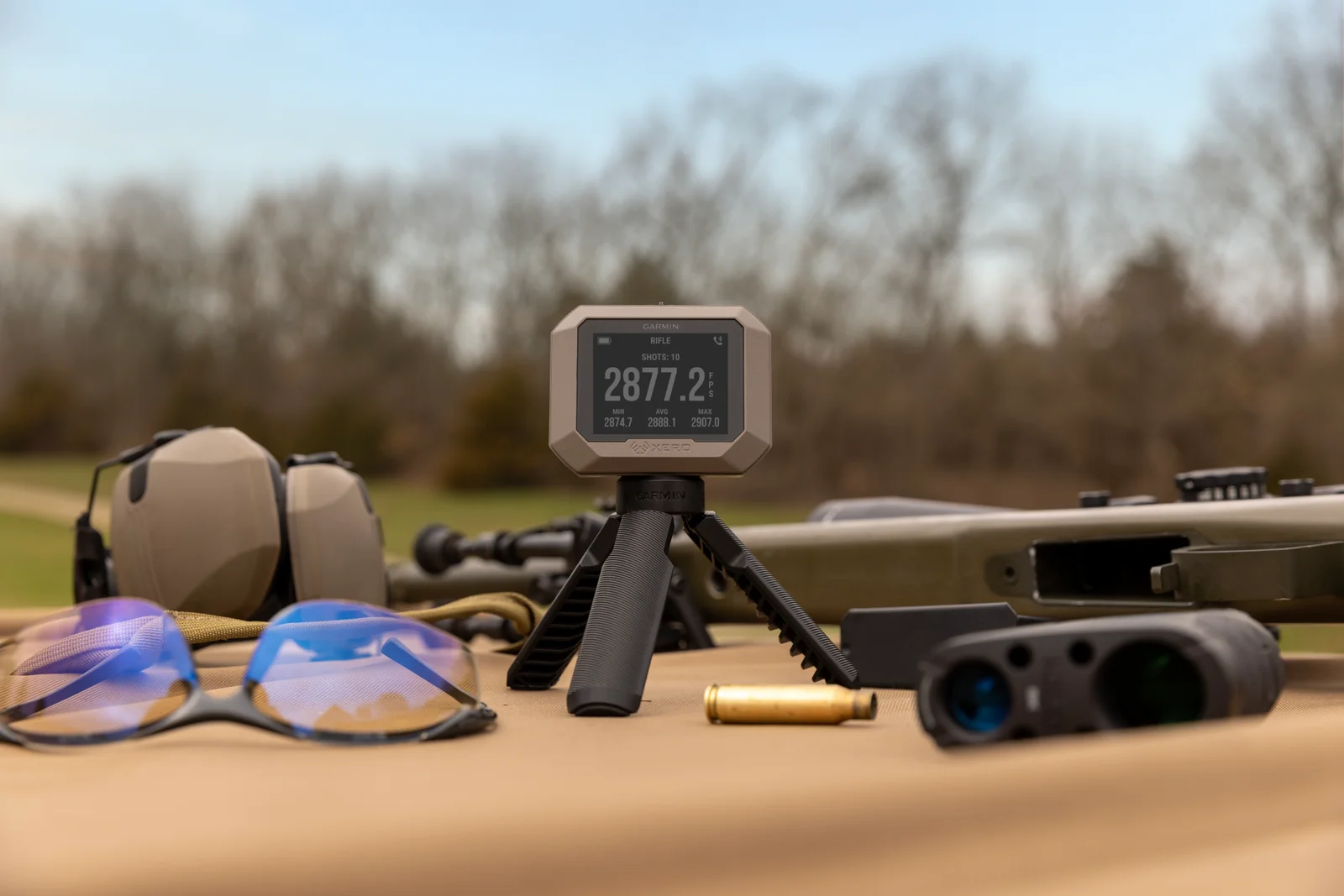 Garmin Xero chronograph on a tripod at a rifle range showing a ten-shot velocity string with min, average, and max values