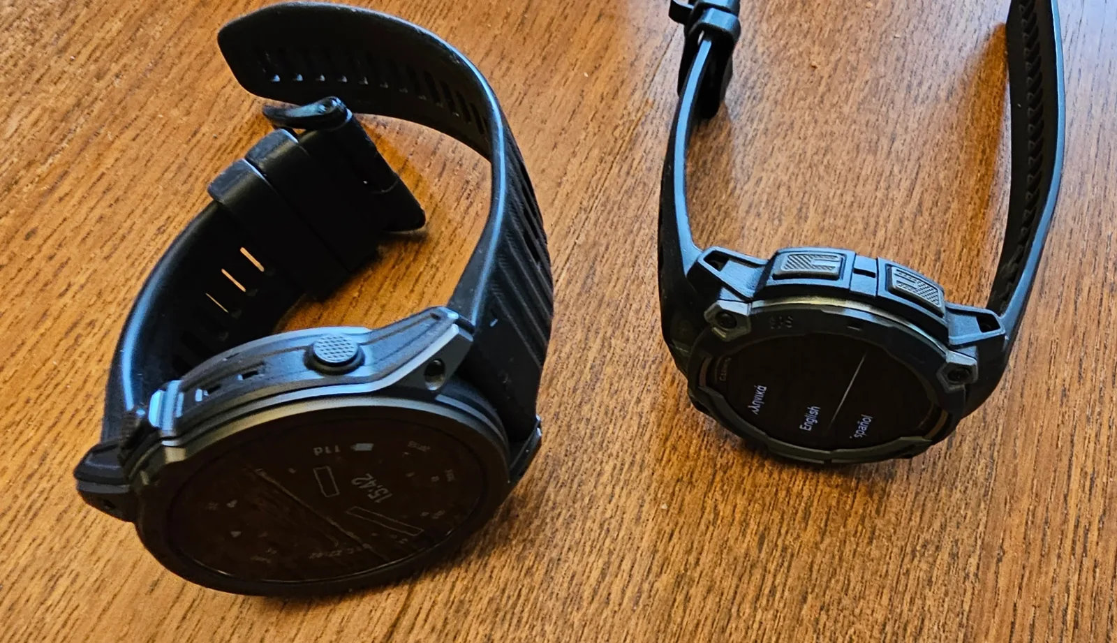 Garmin Instinct 3 AMOLED next to the heavier tactix 7 AMOLED, both shown from behind on a wood table