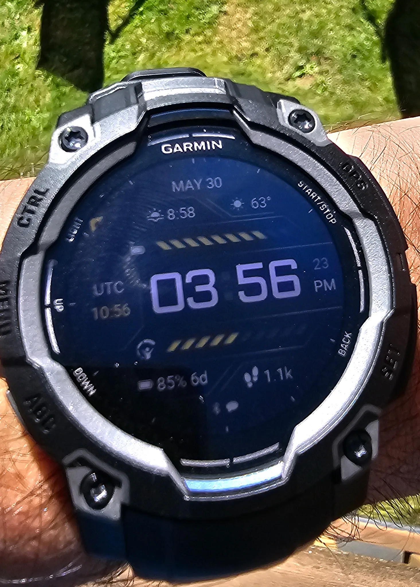 Garmin Instinct 3 AMOLED on the wrist in direct sunlight, display still legible, showing 85 percent battery and 6 days remaining