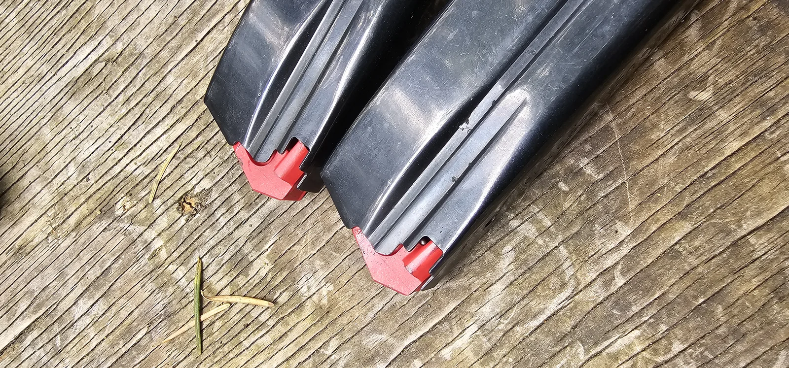 Both HK CC9 magazines on a wood bench showing the red followers, one lifted out of its track