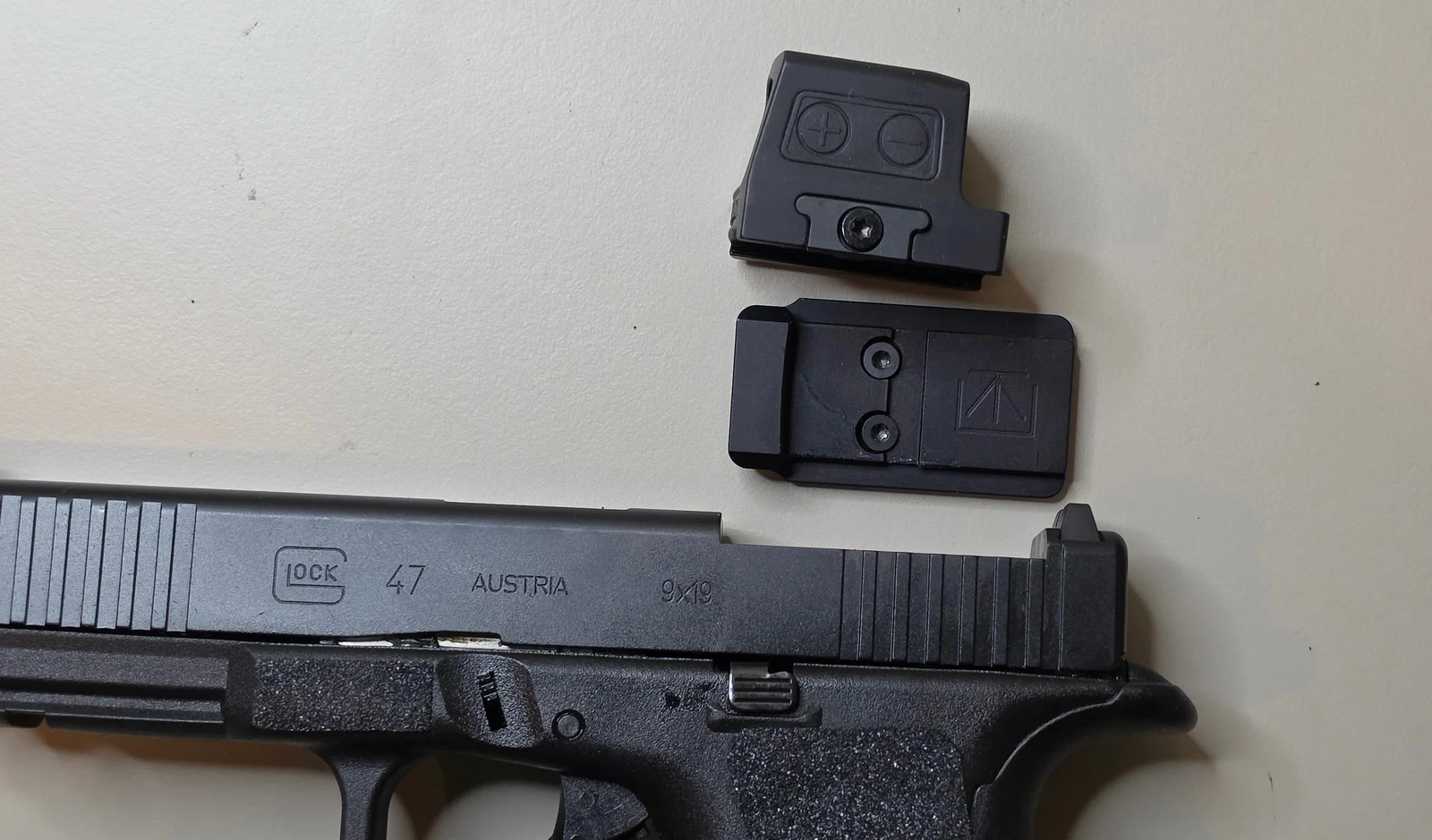 Holosun 509T X2 Gold and its Glock MOS adapter plate laid above a Glock 47 slide, showing the two pieces that stack over the bore