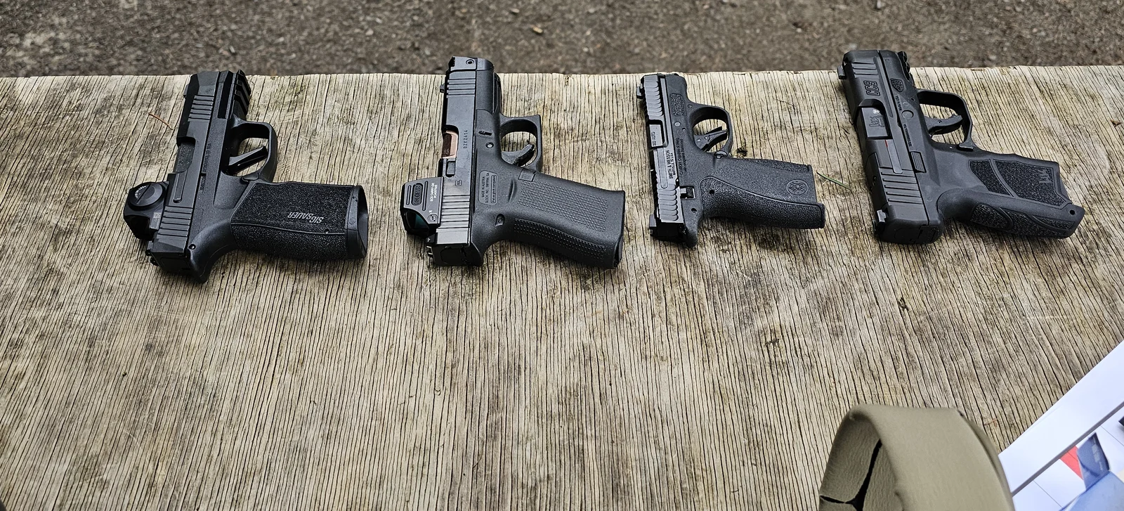 Four slim concealed carry pistols laid out on a wooden range bench, including a SIG P365 and a Glock 43X wearing a Holosun optic