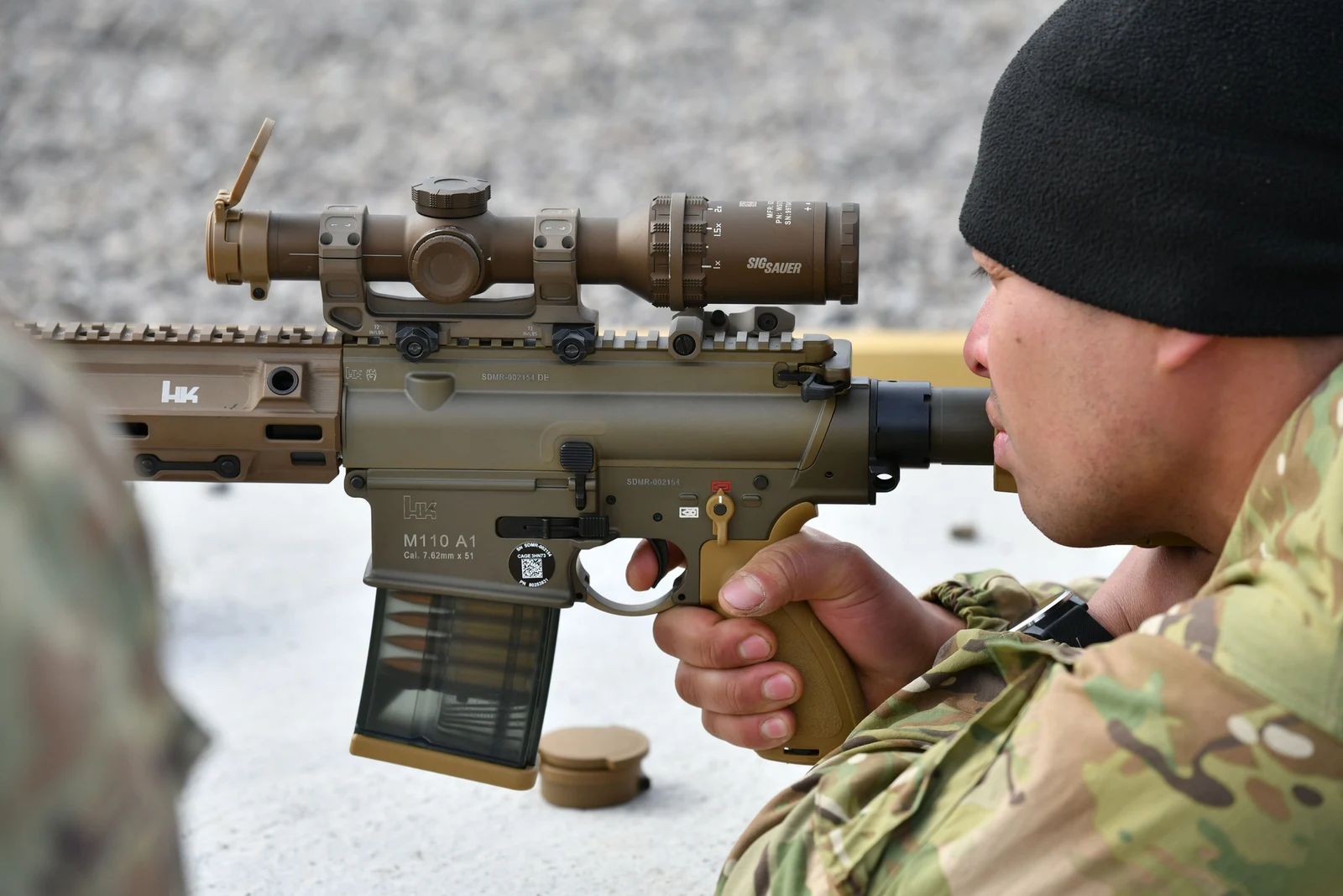 Soldier behind a Heckler and Koch M110A1 rifle with the receiver marked M110 A1 Cal. 7.62mm x 51 and a SIG Sauer low-power variable optic