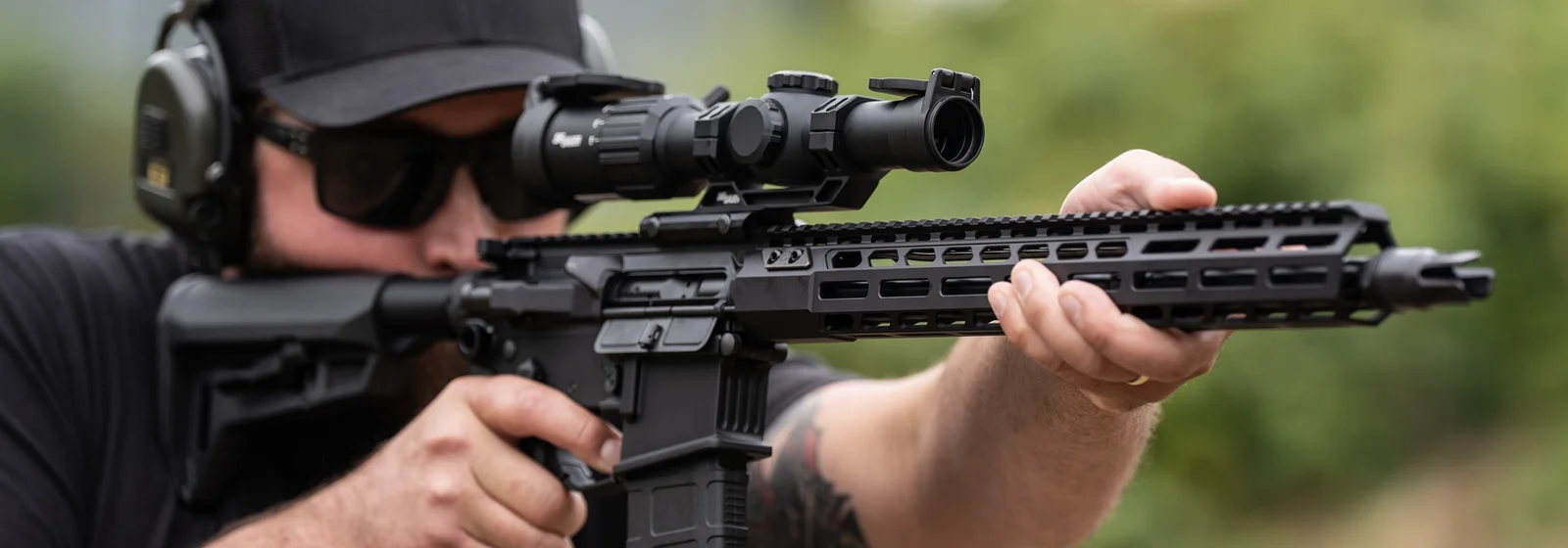 A shooter aiming an AR-15 fitted with a SIG Sauer low-power variable optic with a magnification throw lever