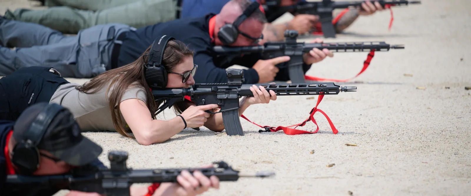 Line of shooters prone on a rifle range firing AR-15 carbines with red slings