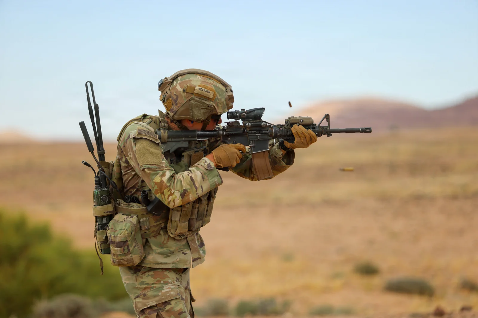 U.S. Army soldier firing an M4 carbine on a desert range with an ejected case in the air
