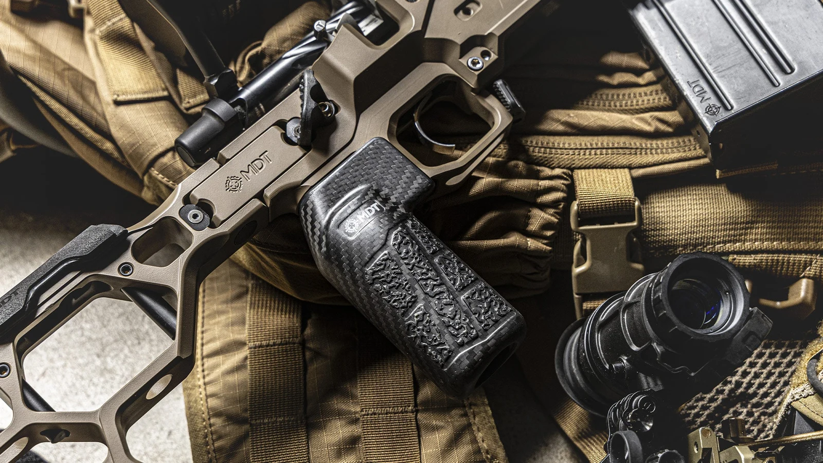 Close-up of an FDE MDT DRT chassis showing the skeletonized magnesium body, trigger guard, and textured carbon fiber vertical grip
