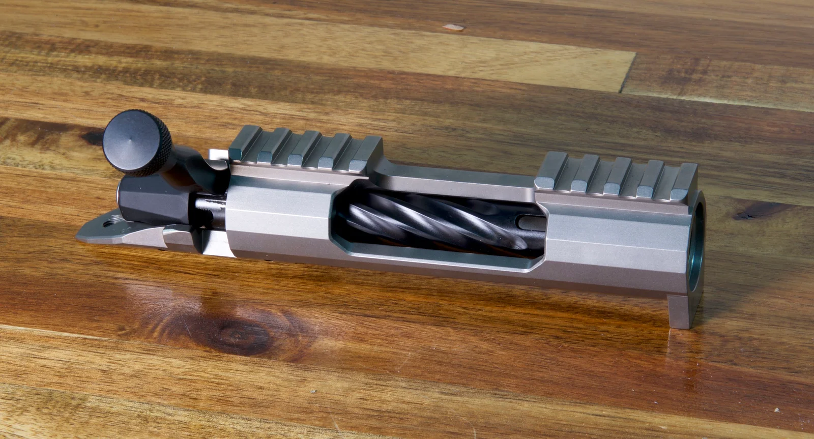 Lone Peak Arms Fuzion action on a wooden bench, showing the split Alpine Port rail with a gap over the ejection port, spiral-fluted bolt, and side bolt release