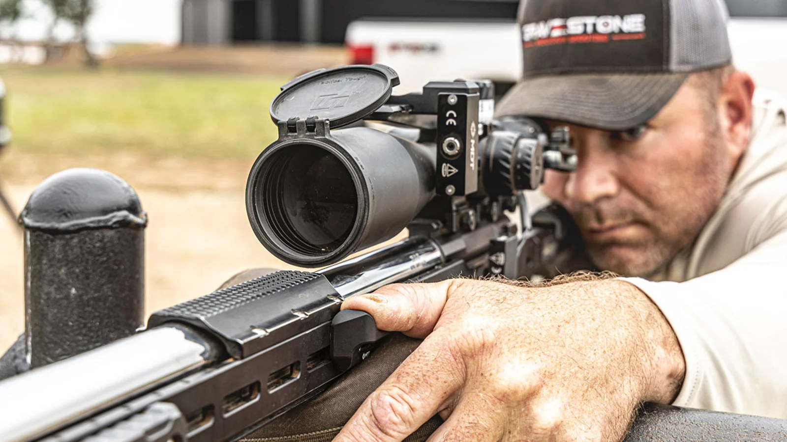 A precision rifle shooter braced off a barricade post, support hand loaded onto the M-LOK forend behind a magnified scope