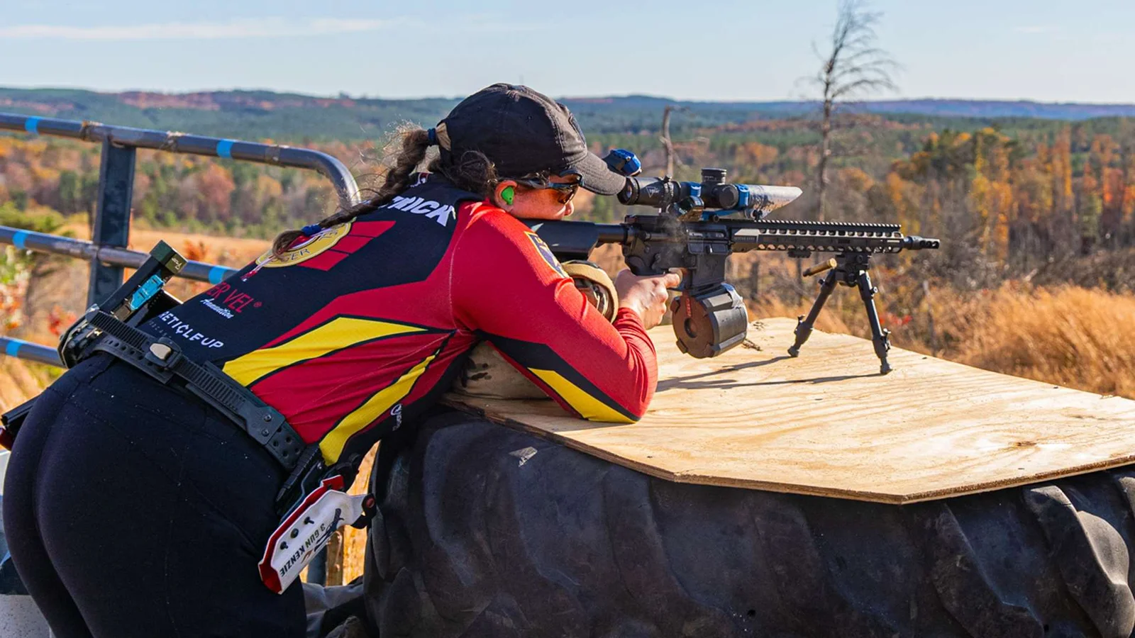 A competitor engaging targets off a plywood prop atop a large tire during a precision rifle match