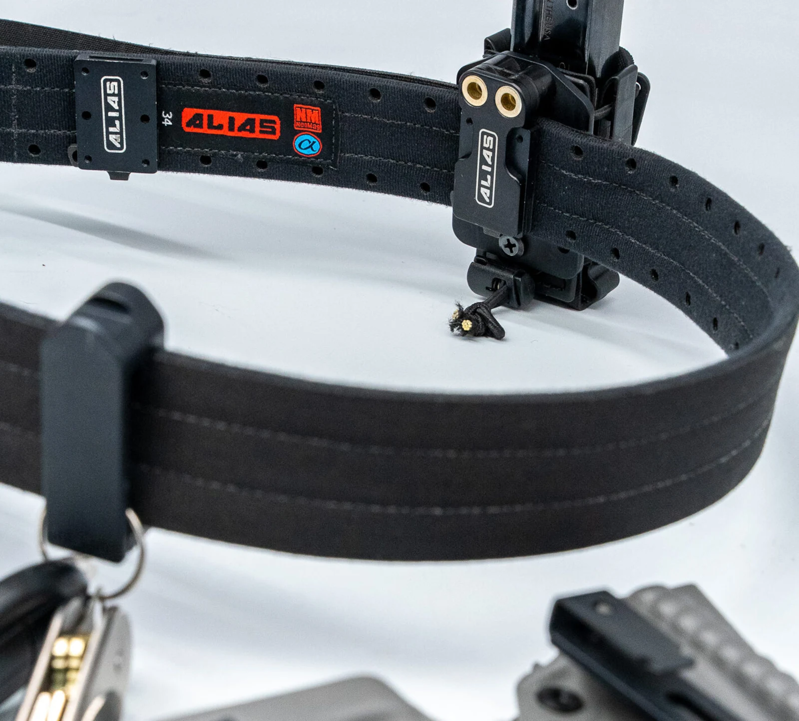 Alias Belt on a white background showing the laser-cut hole pattern, a bolted-on Alias receiver plate, and a magazine carrier clipped to a second receiver