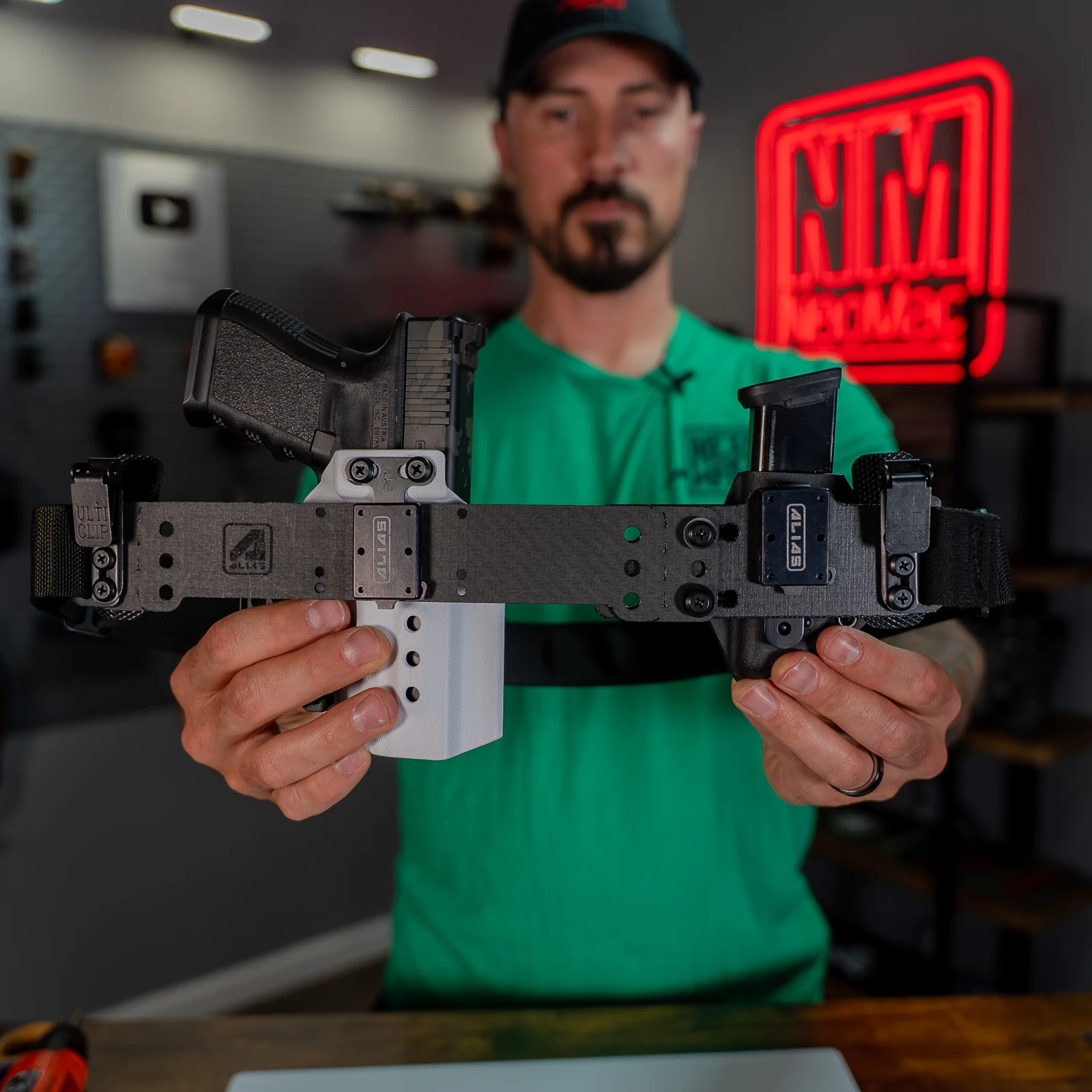 An assembled Alias beltless rig held up in NeoMag's shop, with UltiClips on both ends, Alias receiver plates across the face, a holstered Glock, and a magazine carrier