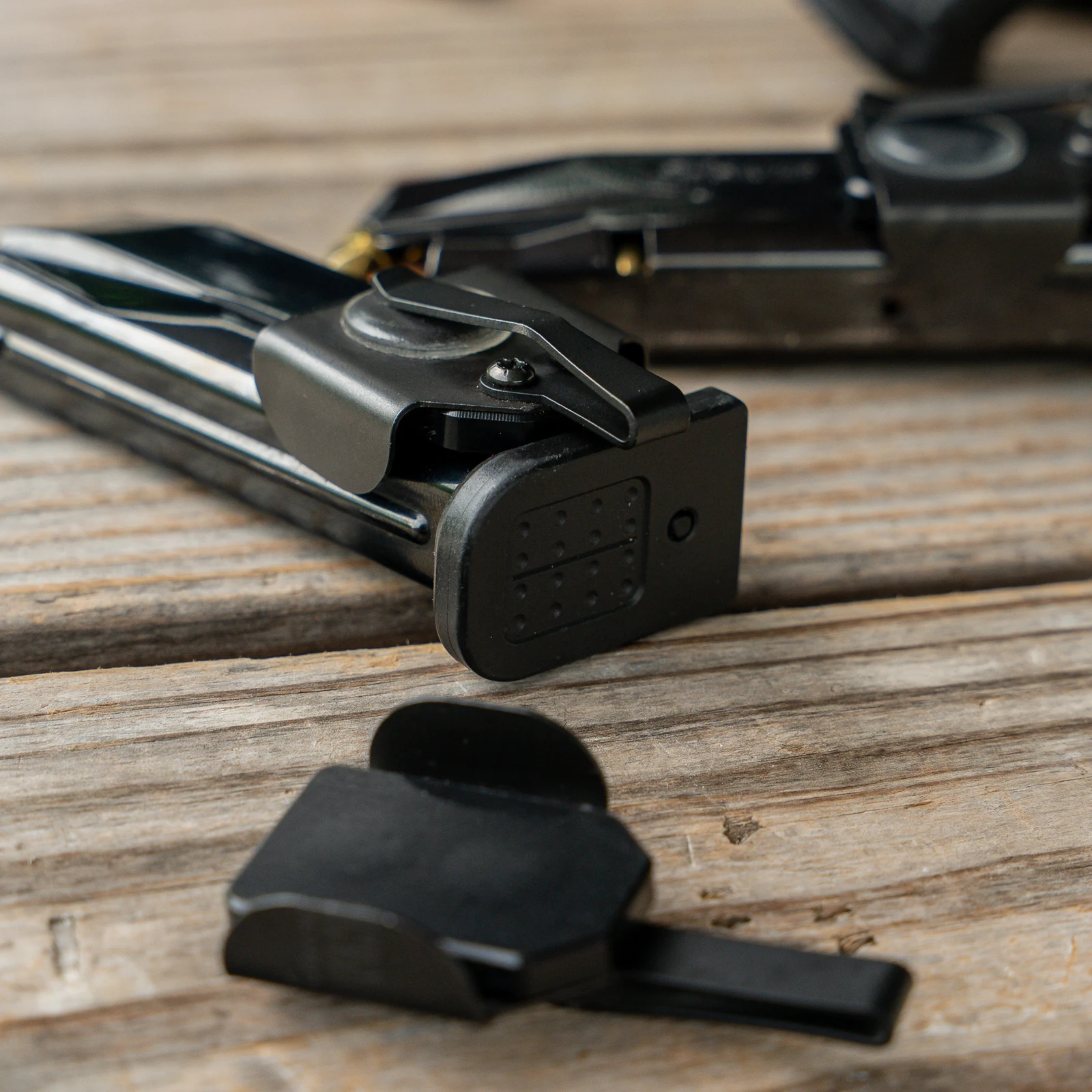 NeoMag Gen 2 carriers clipped to loaded pistol magazines on a weathered wood surface, with a loose carrier in the foreground showing the back plate and pocket clip