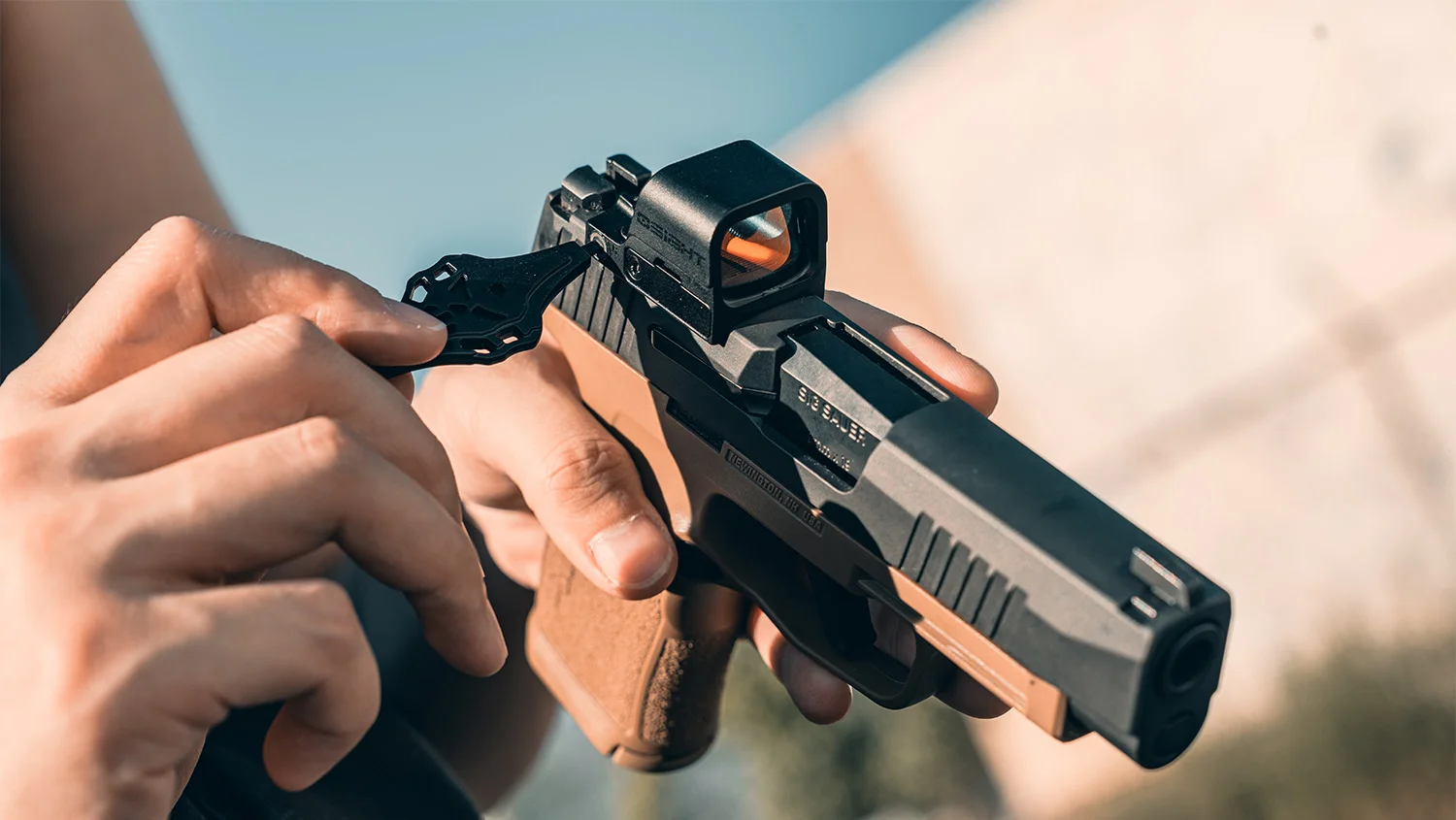 An open-emitter Osight K mounted on a SIG Sauer optics-ready pistol slide held in a shooter's hands outdoors