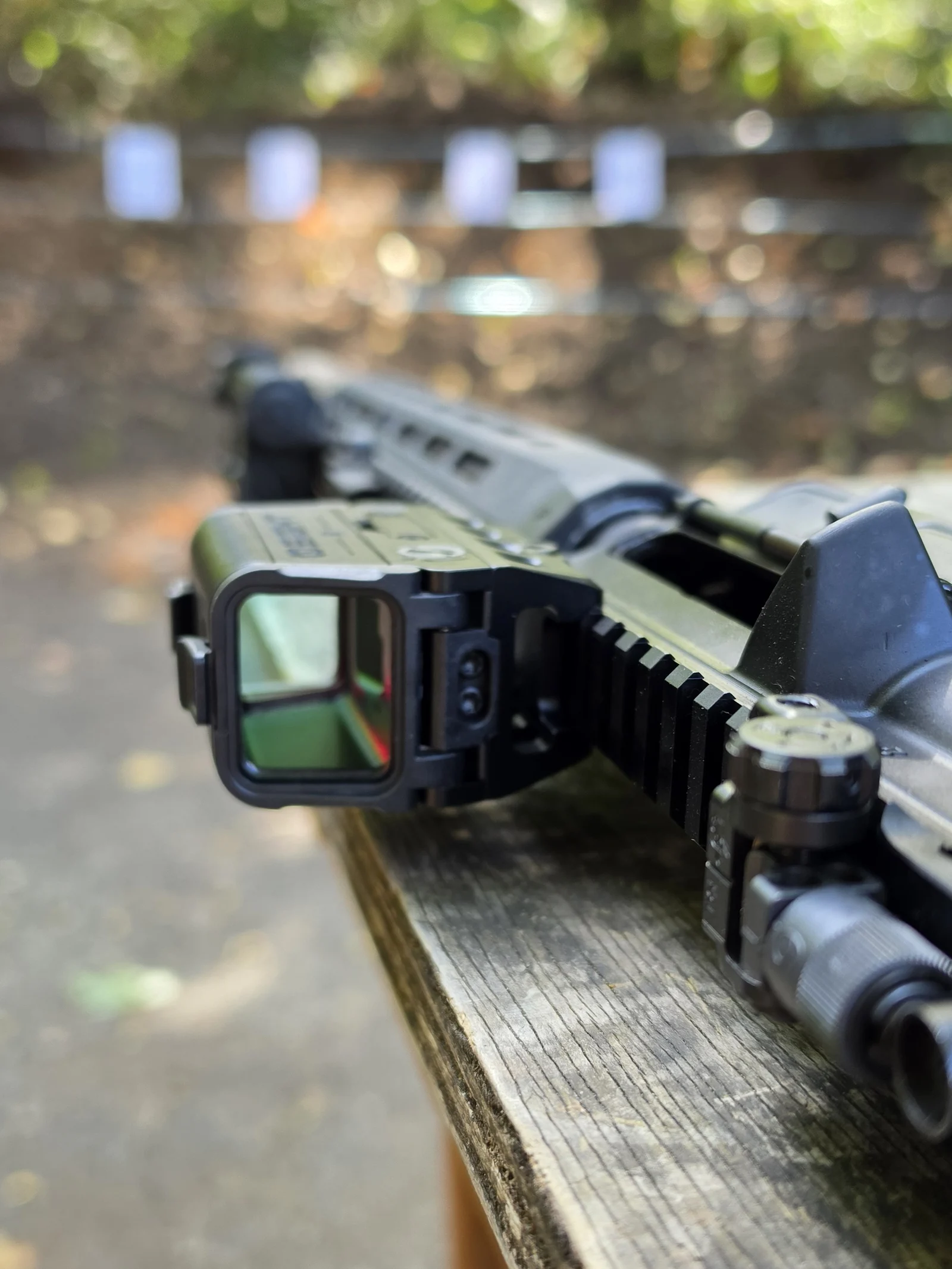 Osight R mounted on a Knight's Armament SR-15 resting on a range bench, seen from the objective end with paper targets downrange