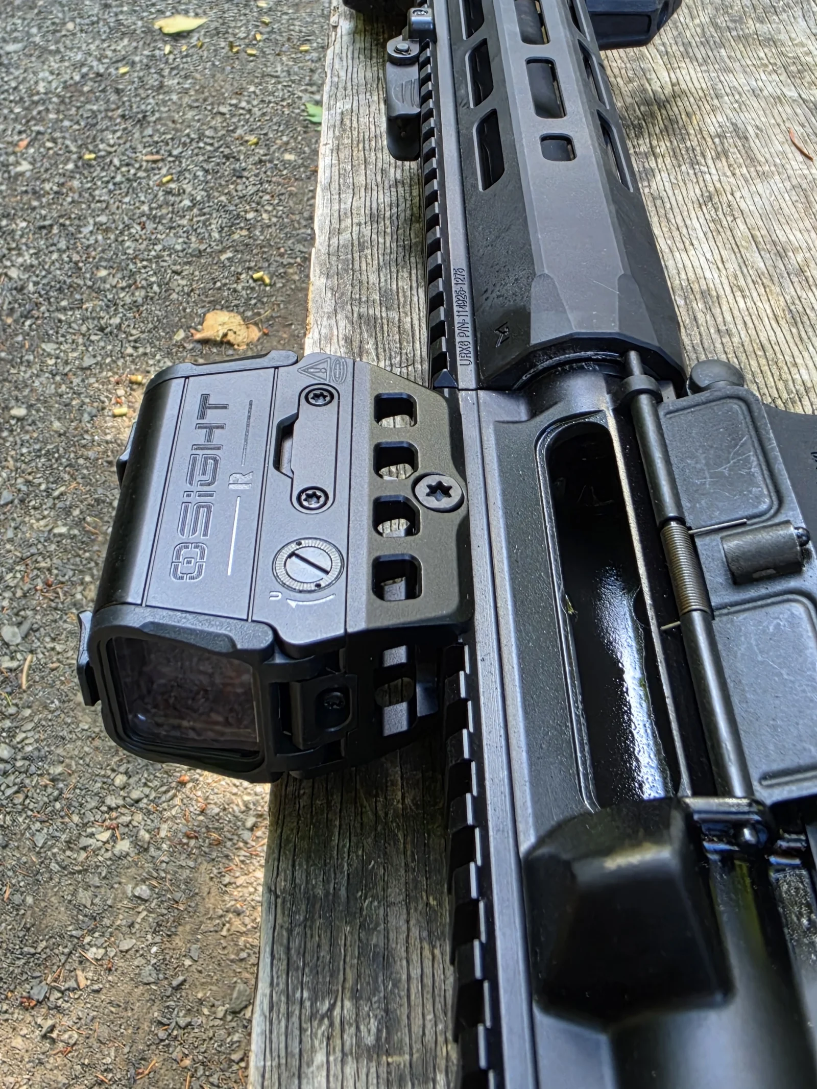 Osight R mounted on the SR-15 lying on a bench, wordmark side up, showing the slotted elevation screw, battery tray, and the four cutouts in the included mount