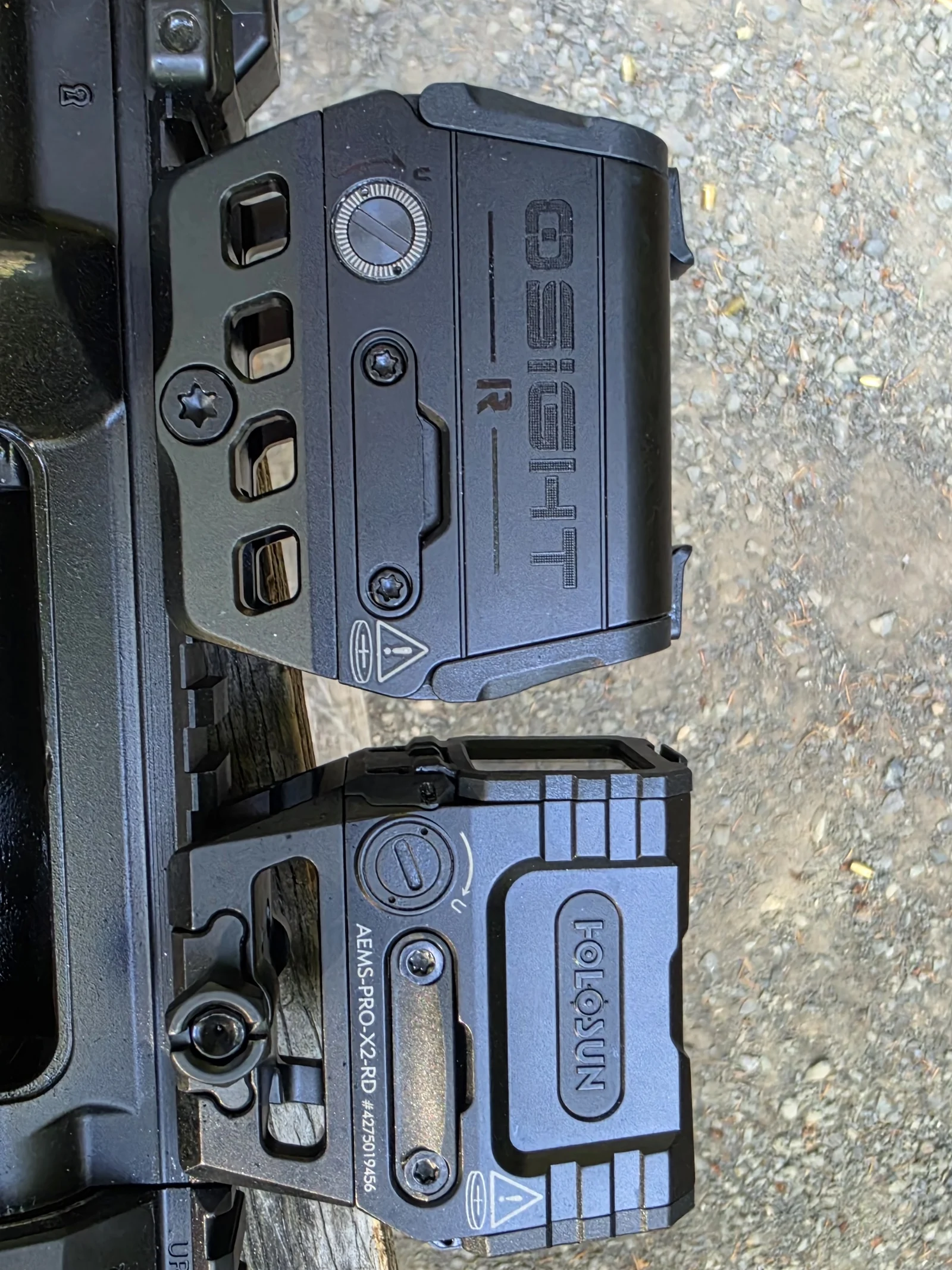 Osight R above and Holosun AEMS Pro X2 below, both on their sides on a bench, comparing housing size and mount design