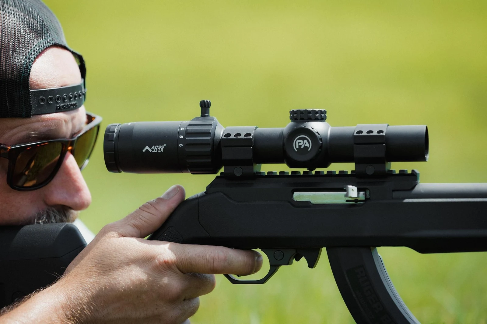 Shooter aiming a Ruger 10/22 equipped with the Primary Arms CLx 1-6x24, with the ACSS .22 LR marking and throw lever visible