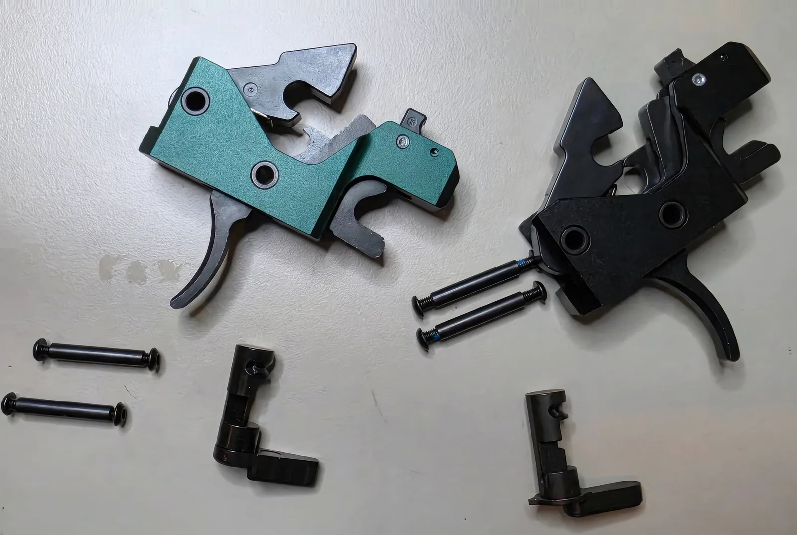 Two Triggered Company Disruptor trigger cassettes on a bench, a green launch unit at left and a black current-revision unit at right, each with two anti-walk pins and a safety selector beside it